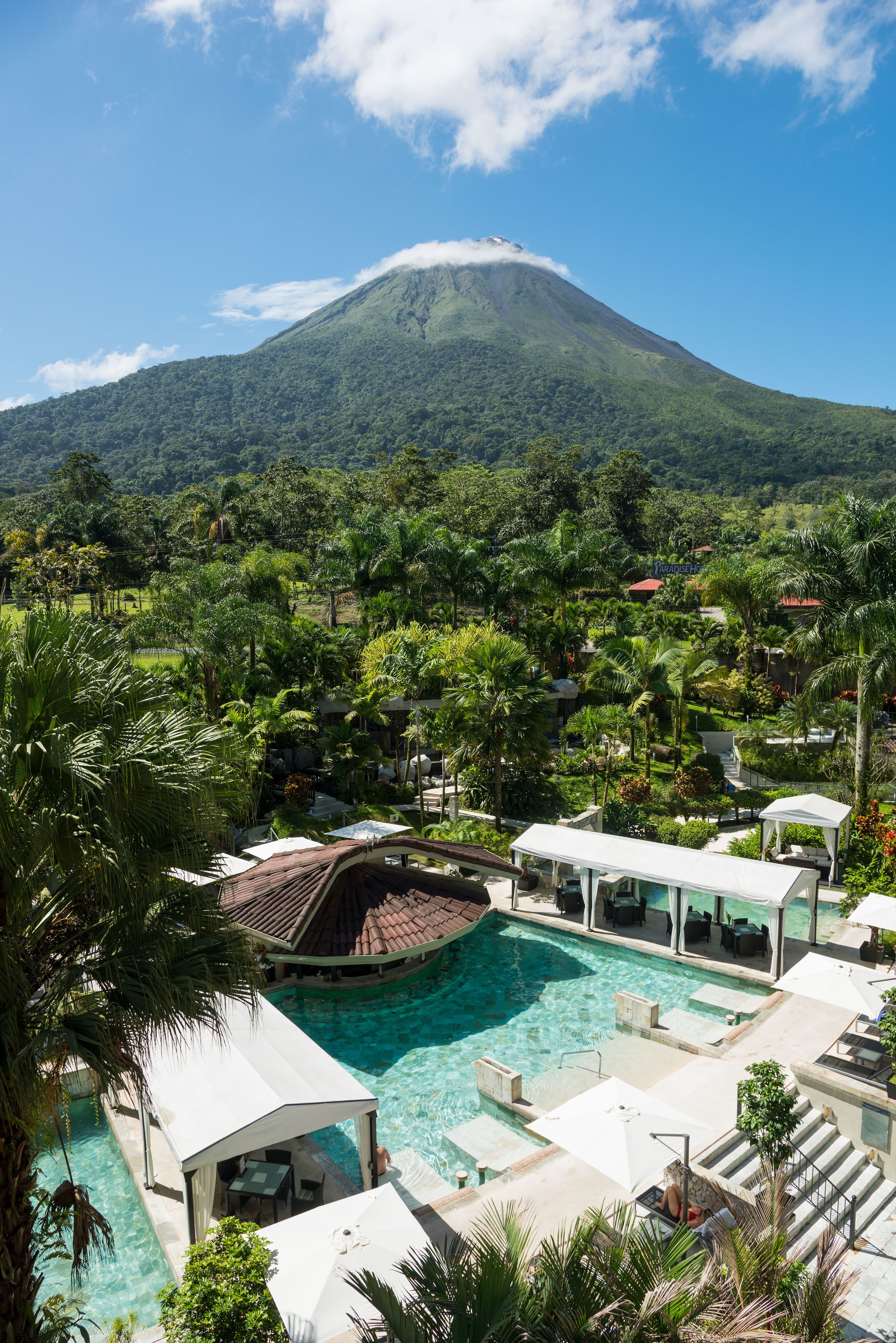A resort with a swimming pool, lounge areas, and a view of a mountain.