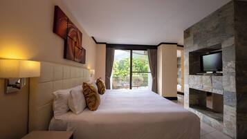 Een hotelkamer met een groot bed, een wandtelevisie, een stenen open haard en een balkon met uitzicht op groen.