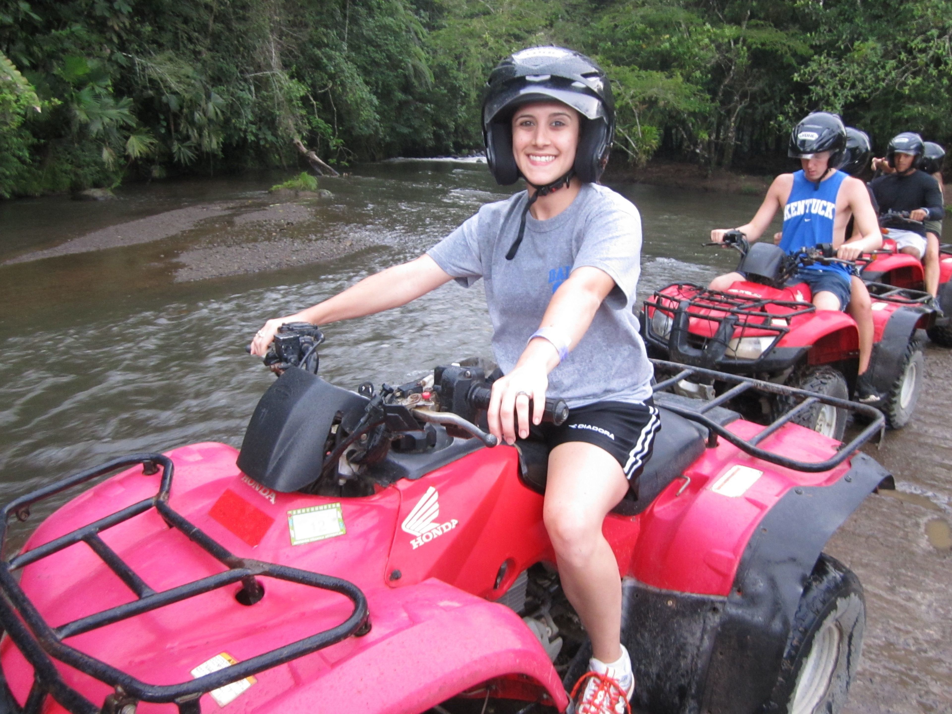A person riding a red ATV on a riverbank.