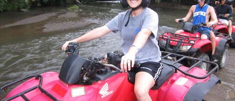 A person riding a red ATV on a riverbank.