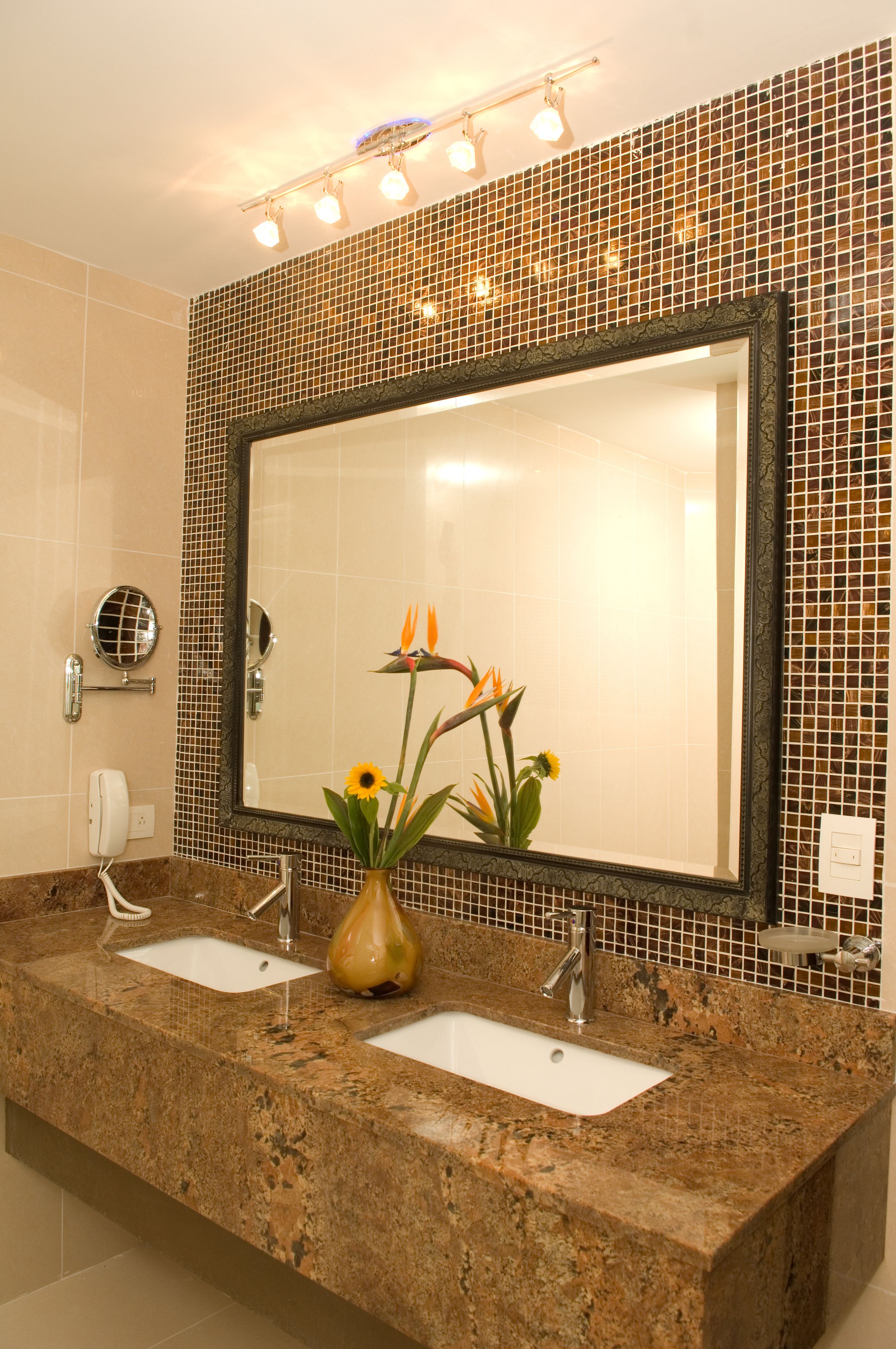 Une salle de bain avec deux lavabos, un grand miroir et un vase décoratif orné de fleurs.