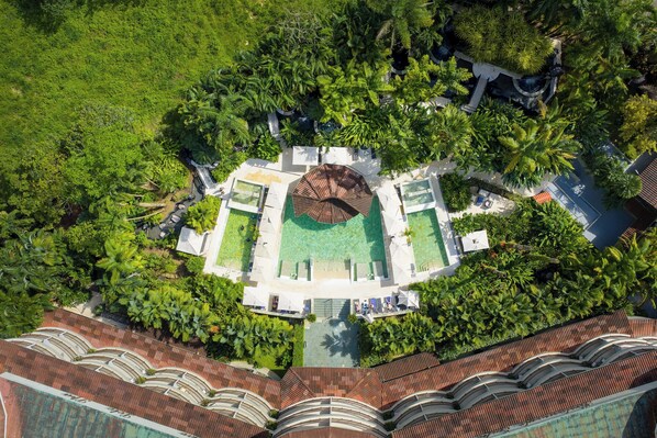 Vista aérea de un resort con piscina central, rodeado de exuberante follaje y palmeras.