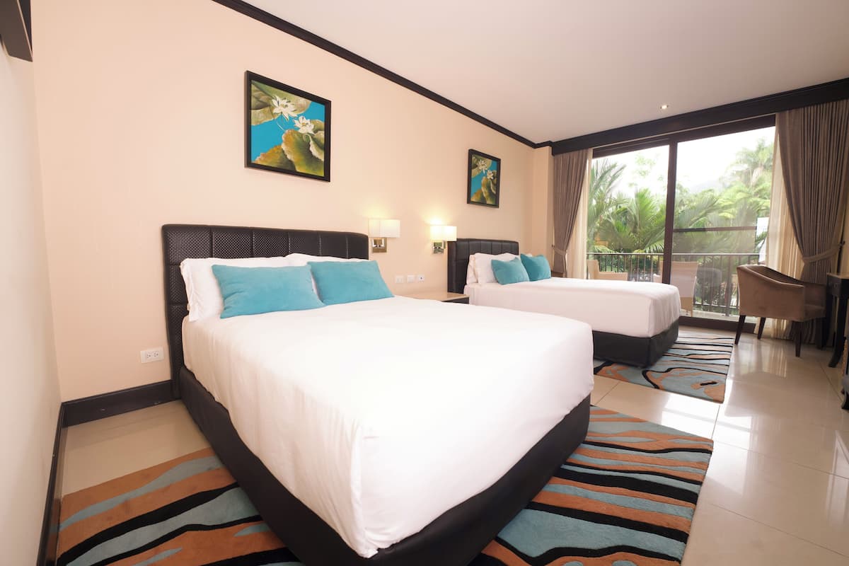 A hotel room with two beds, a balcony with a view of palm trees, and artwork on the walls.