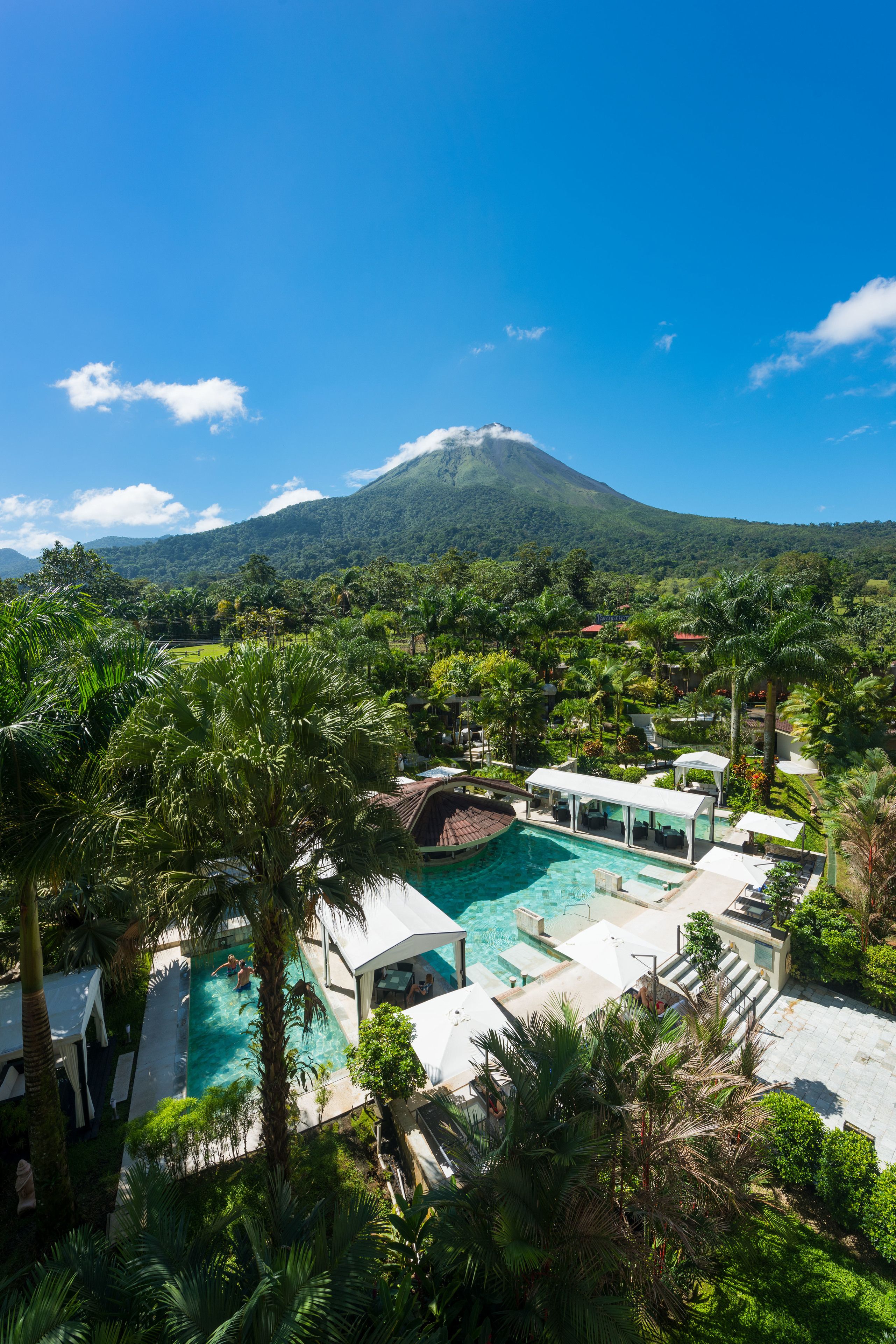 A resort with a swimming pool, palm trees, and a mountain in the background.