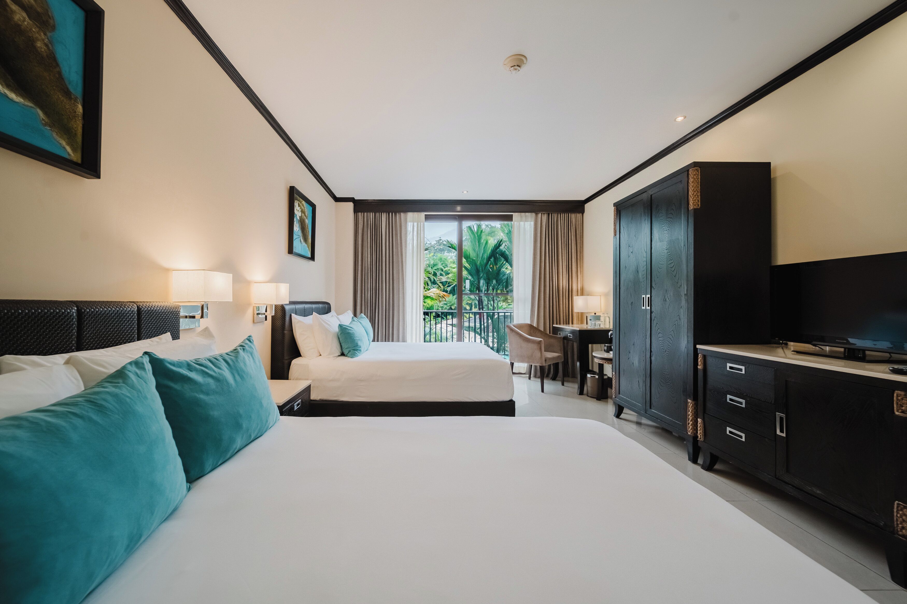 Habitación de hotel con una cama grande, un escritorio, un televisor y un balcón con vistas a zonas verdes.