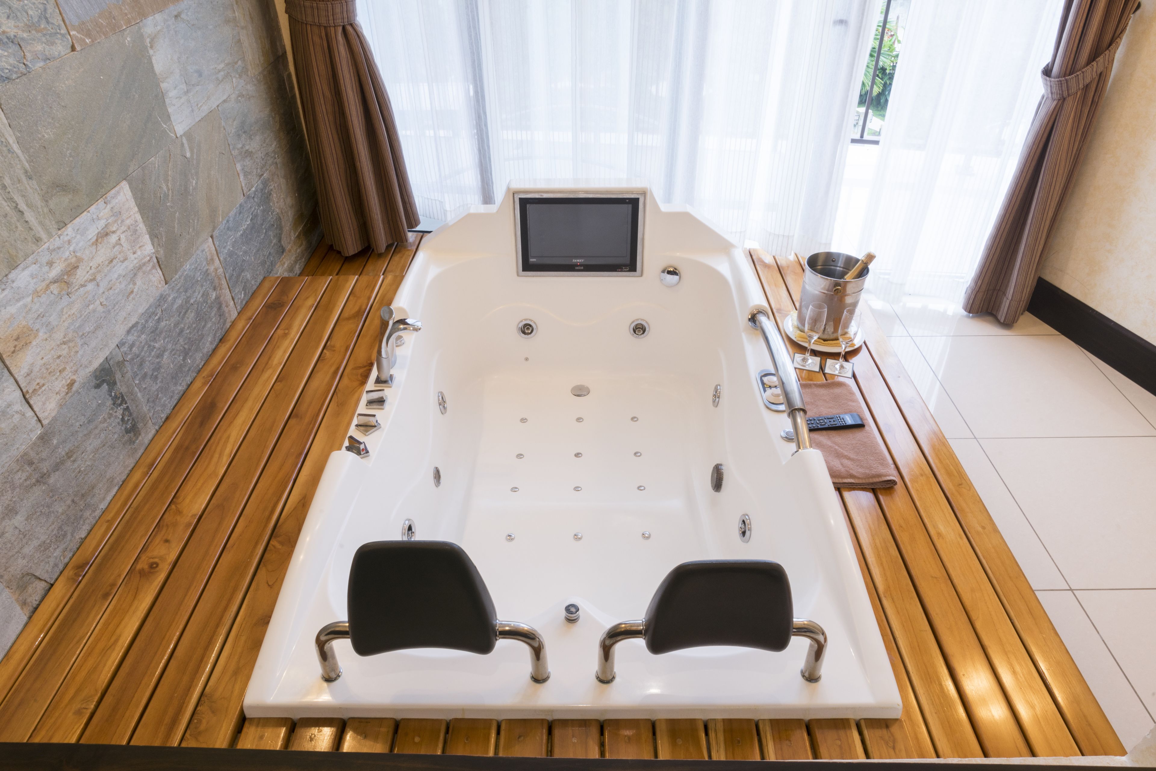 A modern spa area with a wooden floor, a large bathtub, and a control panel.