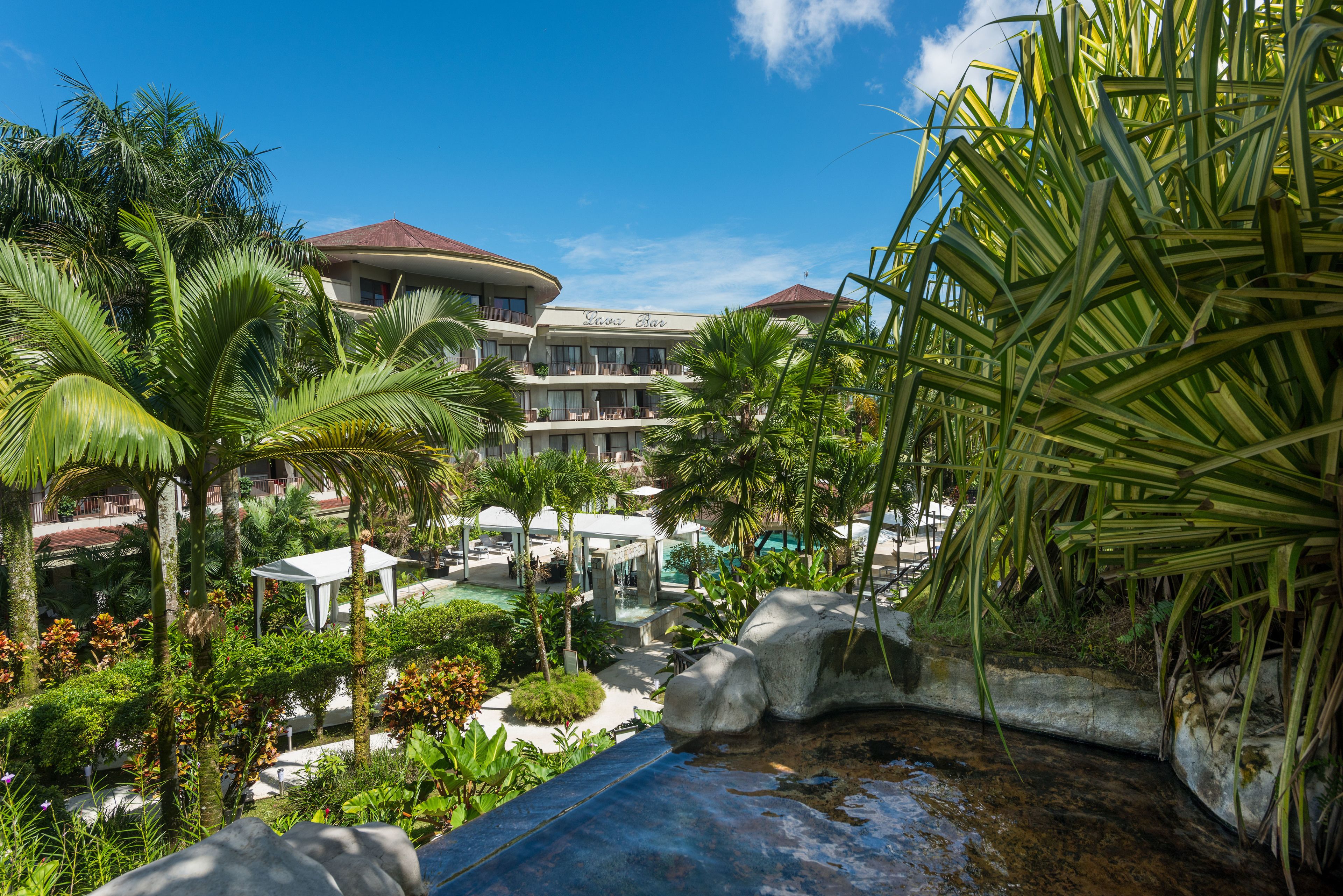 Ein Resort mit Poolbereich, Palmen und einem Geb äude mit rotem Dach.