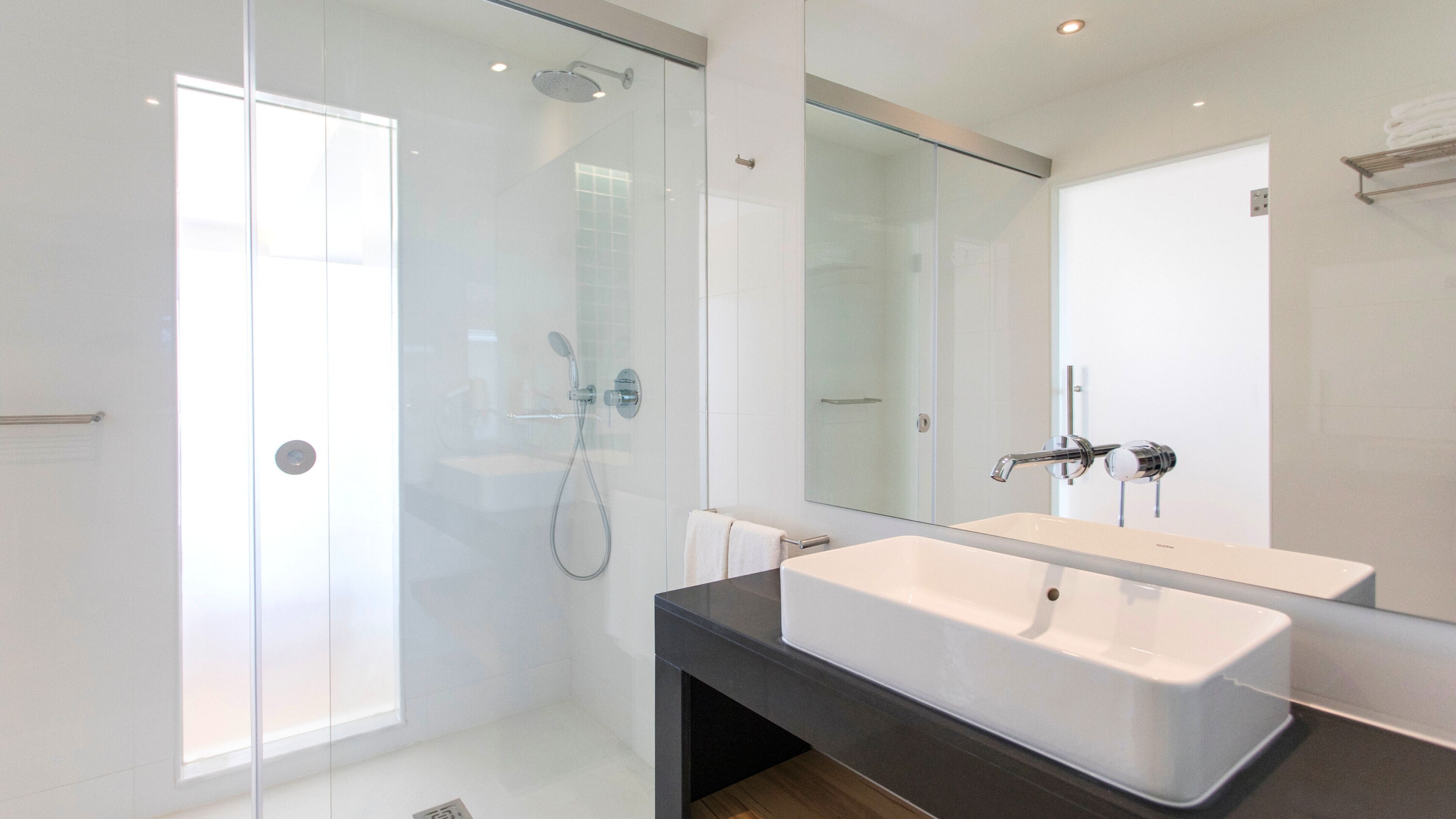 A modern bathroom with a glass shower enclosure, a large mirror, and a dual sink vanity.