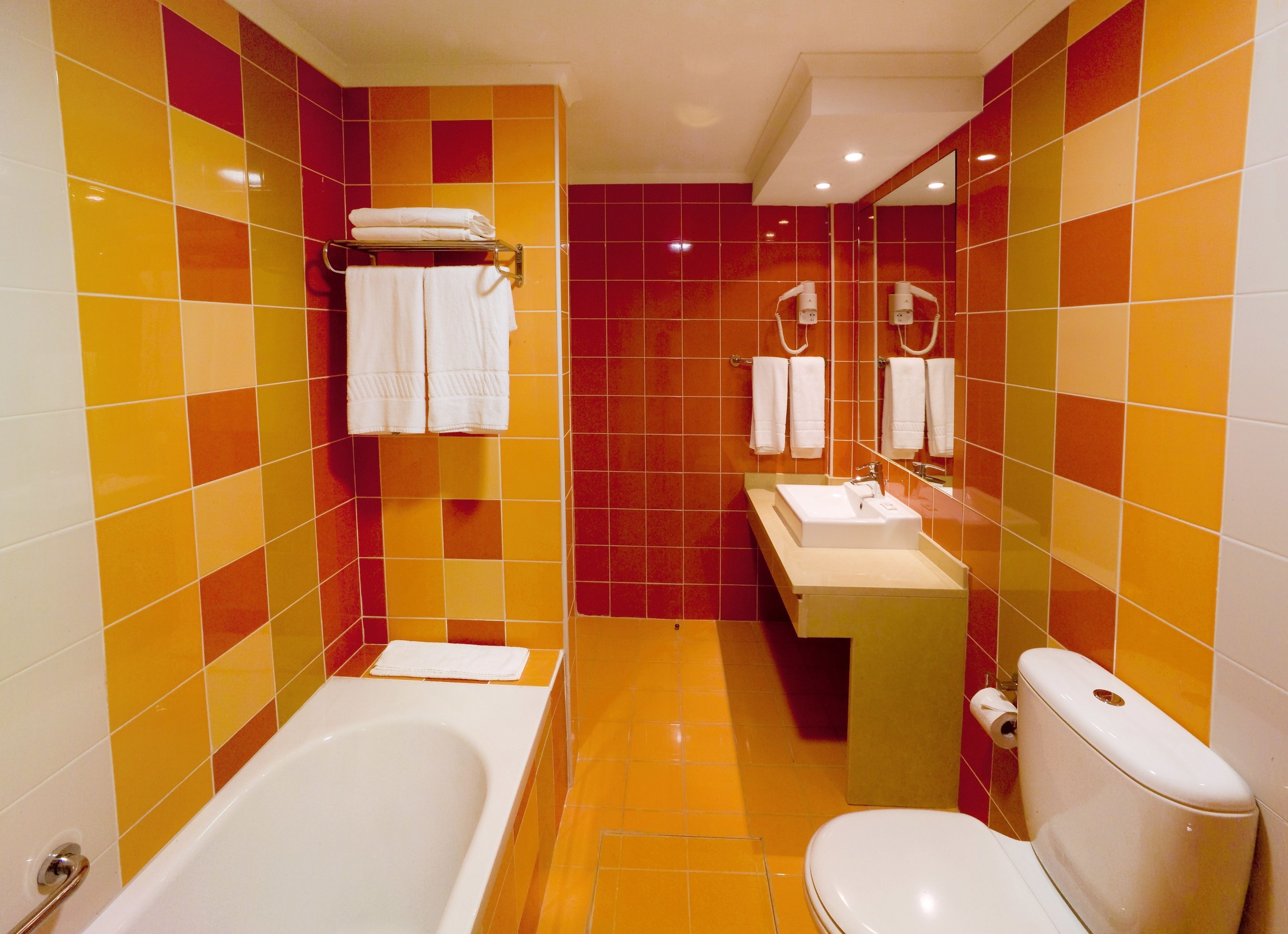 Un baño con bañera, inodoro y lavamanos, con azulejos naranja y rojos.