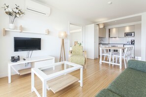 Una sala de estar moderna con un televisor de pantalla plana, una mesa de centro blanca, un sofá verde y un comedor con una mesa y sillas blancas.