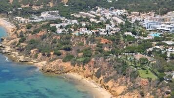 An aerial view of a coastal town with beachfront properties, dense greenery, and a mix of residential and commercial buildings.