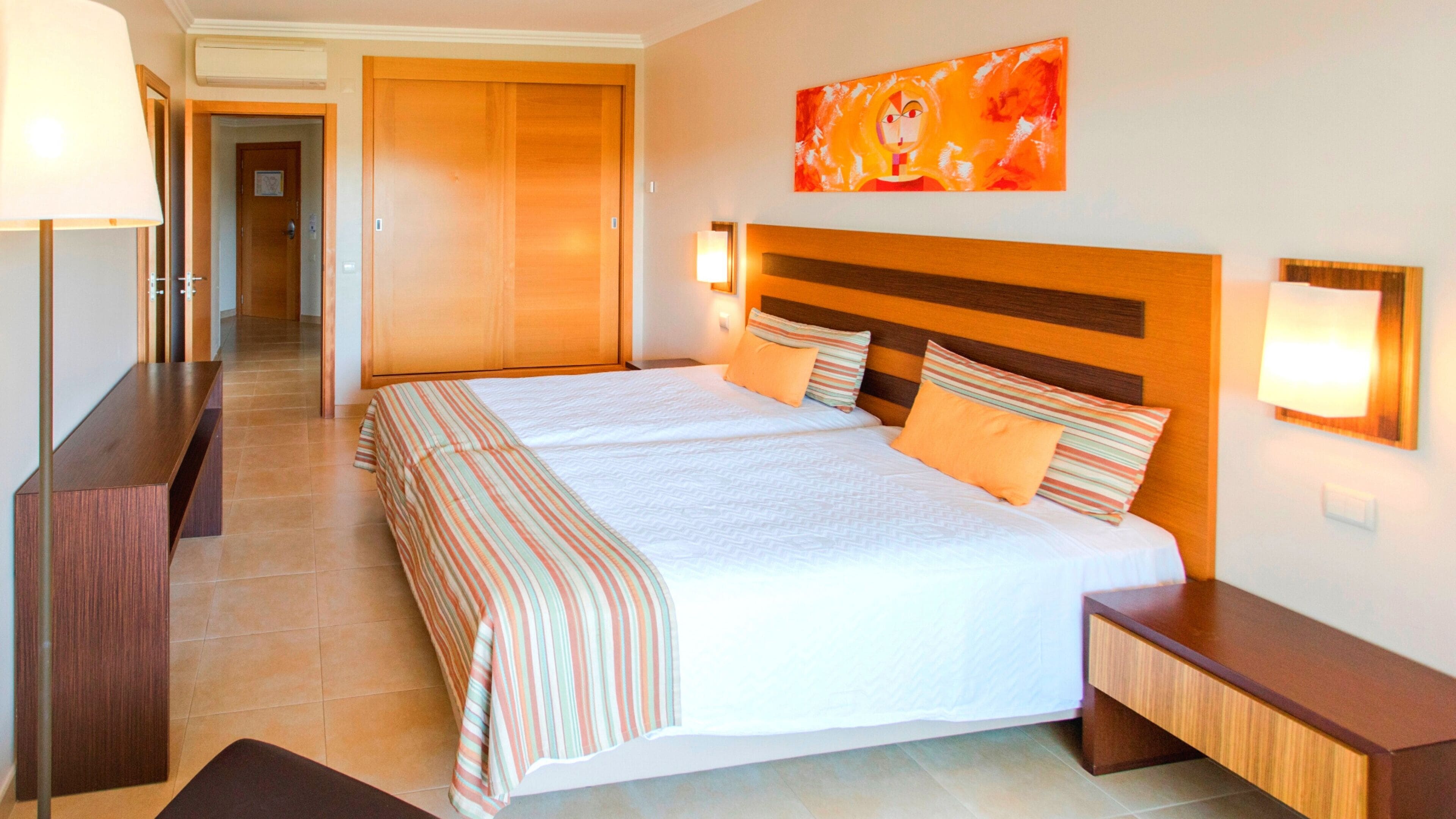 Un cuarto de hotel con una cama grande, un cabecero de madera, dos mesitas de noche, una lámpara y un cuadro en la pared.