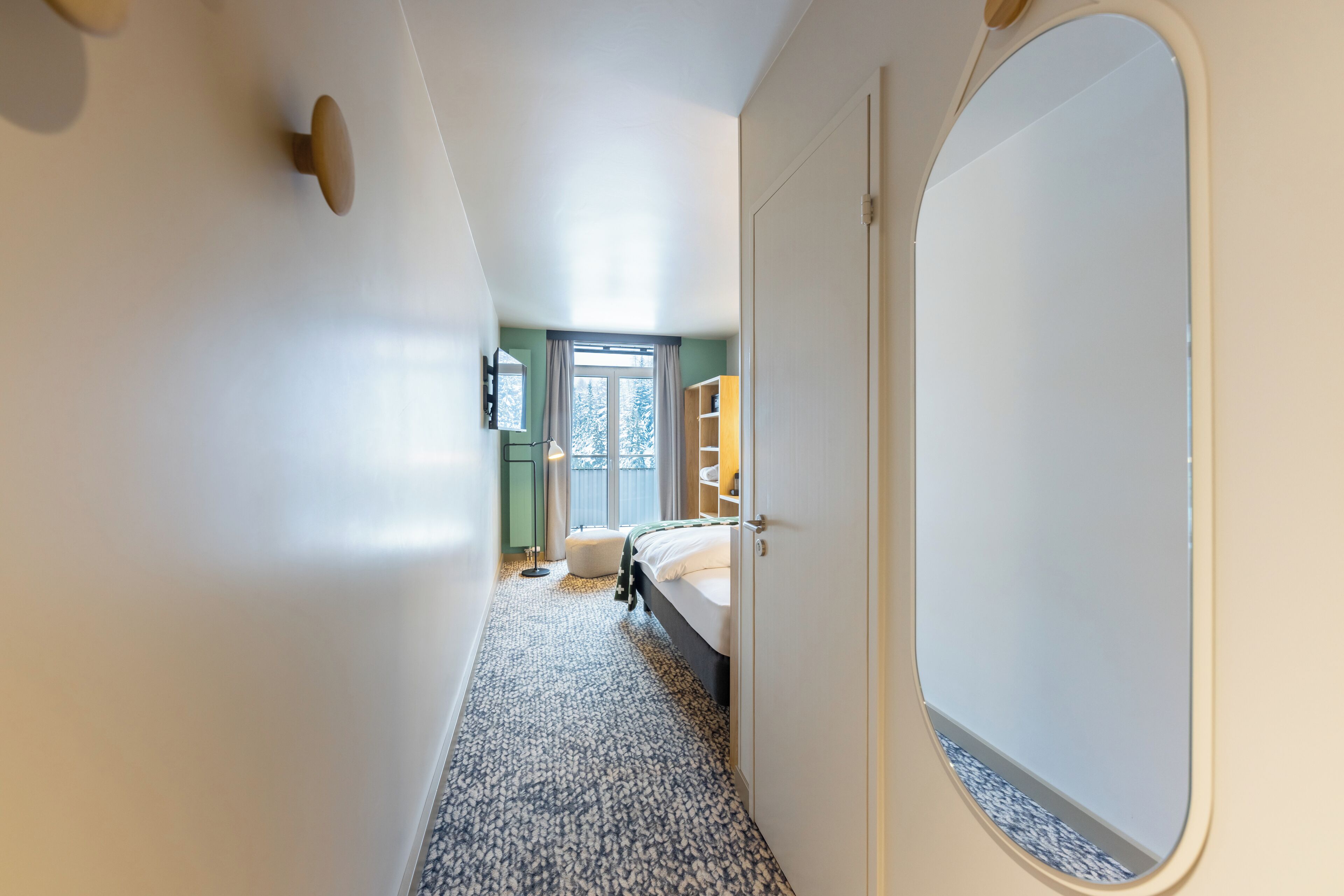 Un pasillo estrecho que lleva a un dormitorio con cama, armario y ventana con cortinas.