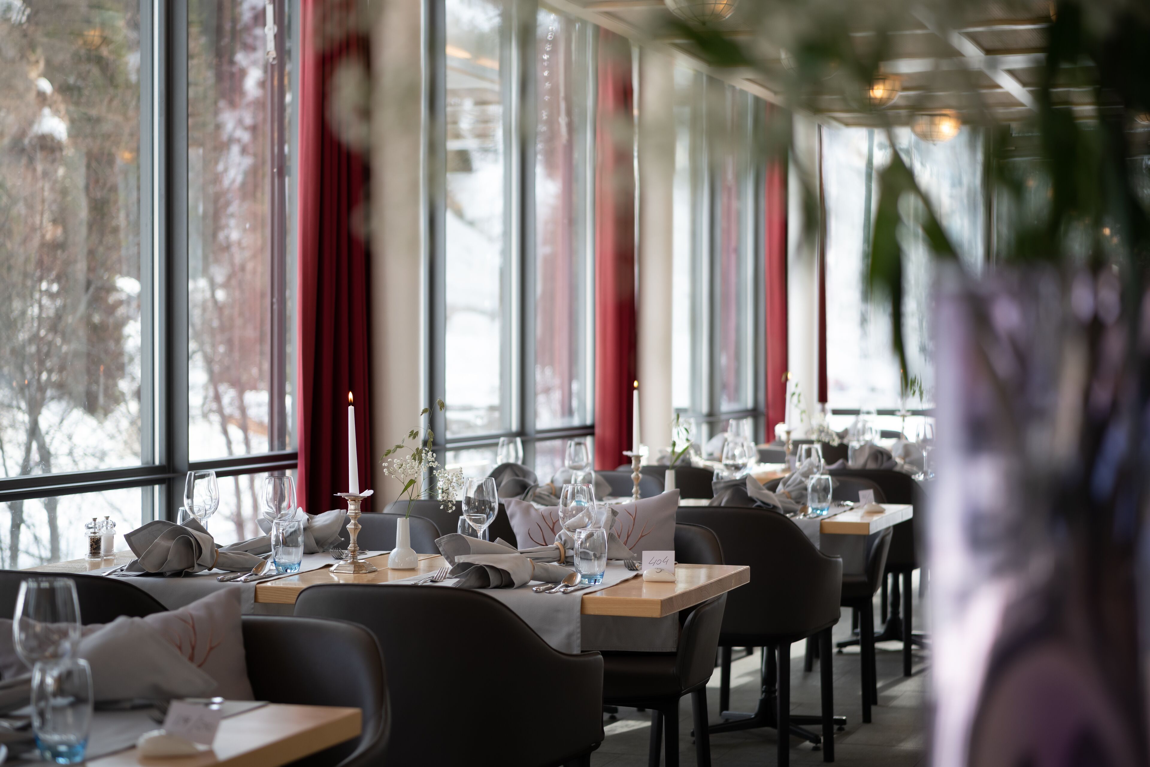 Un restaurante con mesas dispuestas para comer, ventanas amplias y cortinas rojas.