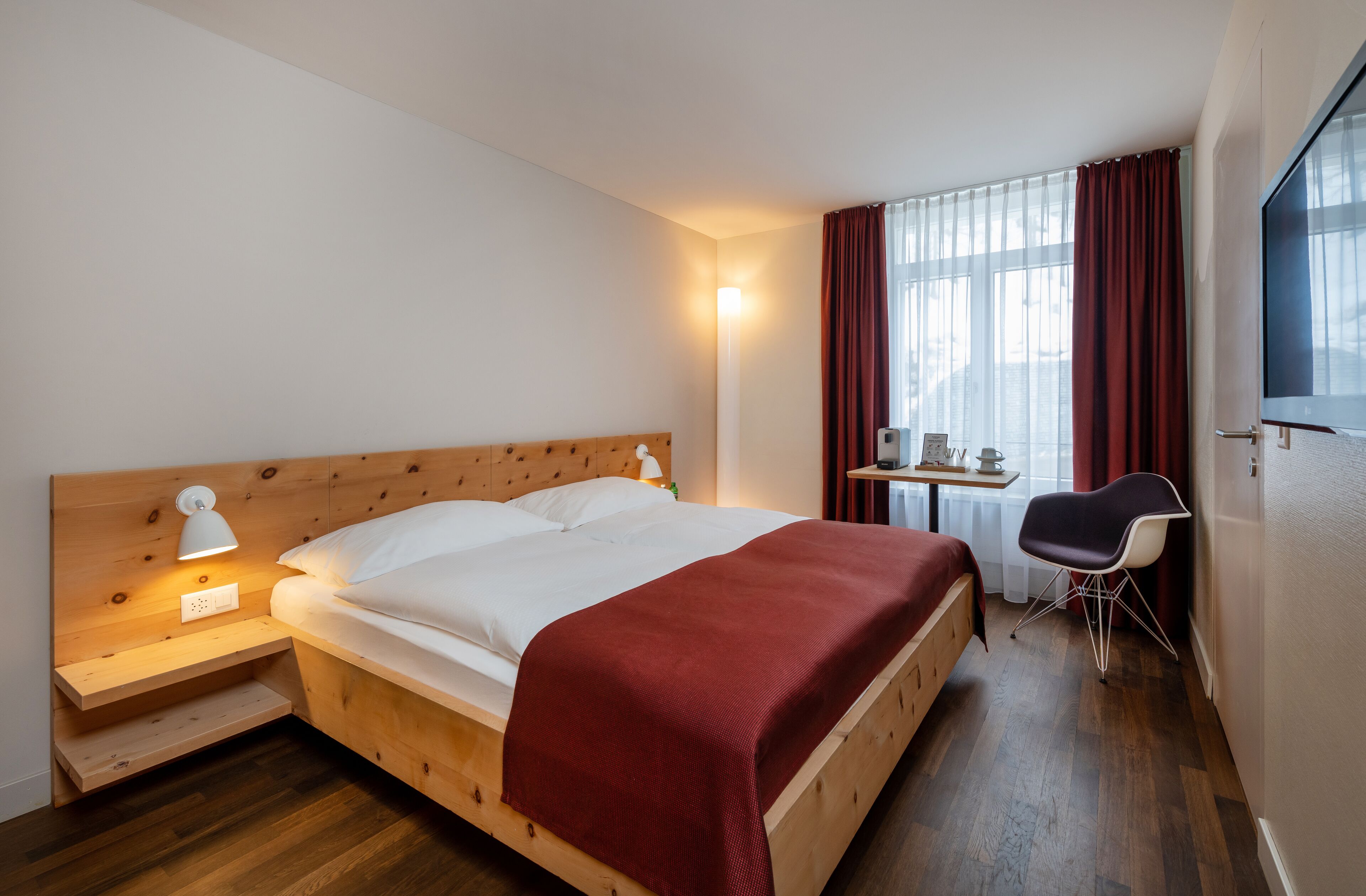 A neatly arranged hotel room with a wooden bed, a desk, a chair, and a TV.