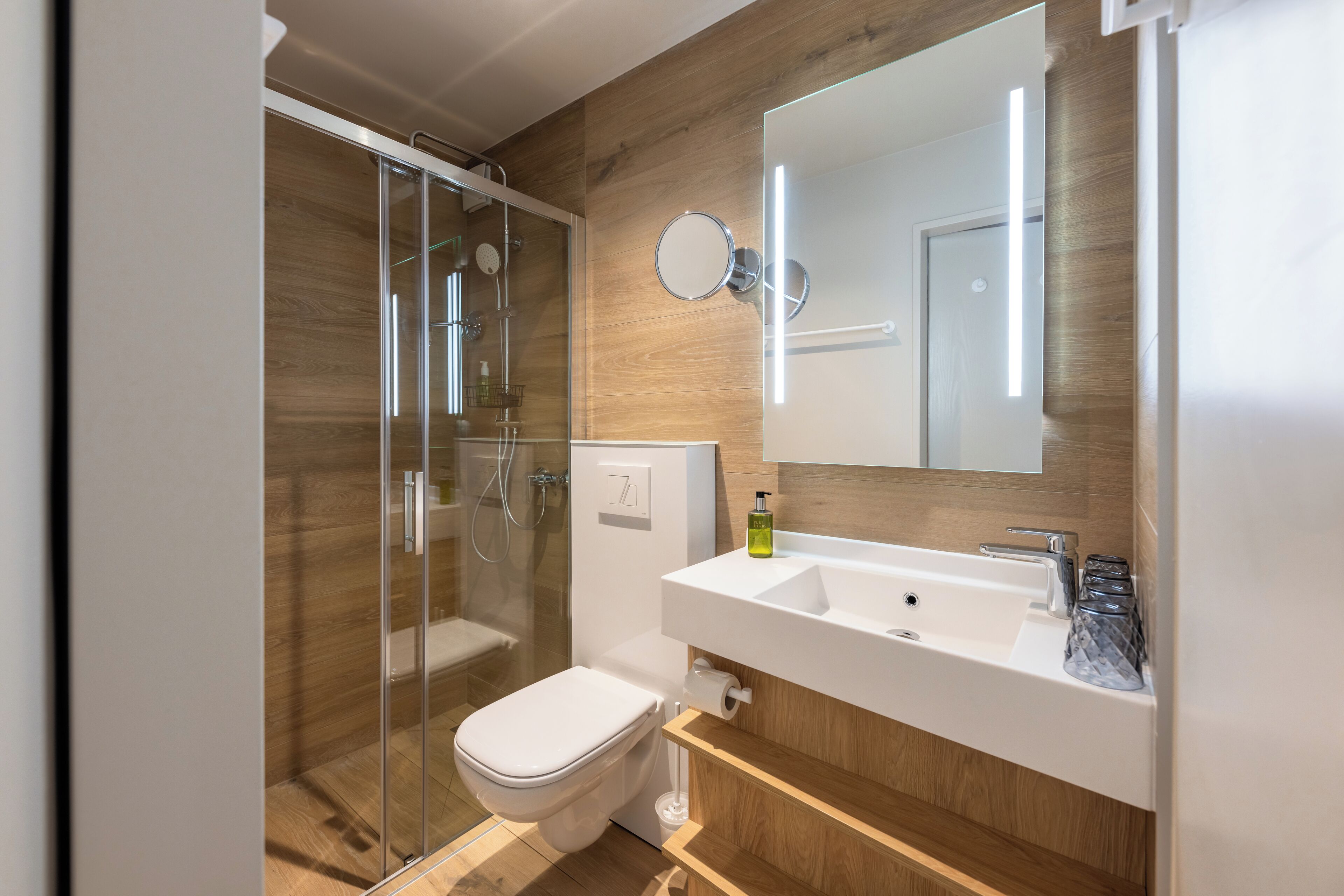 Ein modernes Badezimmer mit einer gläsernen Duschkabine, einem weißen Waschbecken mit Spiegel und Holzvertäfelung.