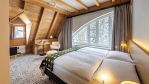 Un dormitorio con una cama grande, un escritorio, una silla y una ventana con vistas a árboles.
