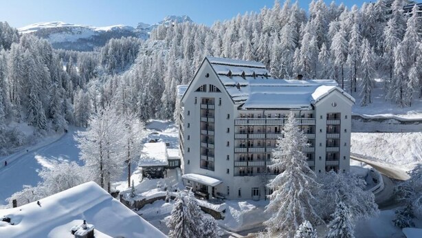 A multi-story hotel with a symmetrical facade, surrounded by snow-covered trees and mountains in the background. - Schweizerhof Sils Maria, a Faern Collection Hotel (Sils im Engadin-Segl)