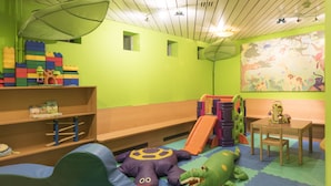 Sala de juegos infantil con tobogán, colchonetas acolchadas y juguetes coloridos.