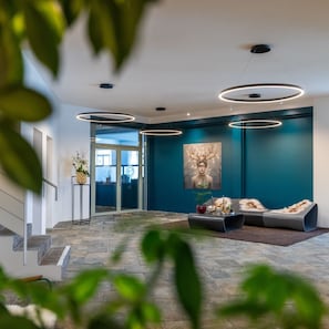A modern interior with a teal accent wall, a large abstract art piece, and a seating area with a fur throw. - Schweizerhof Sils Maria, a Faern Collection Hotel (Sils im Engadin-Segl)