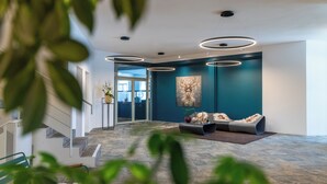 A modern lobby with a staircase, a seating area with cushions, and a large wall painting. - Schweizerhof Sils Maria, a Faern Collection Hotel (Sils im Engadin-Segl)