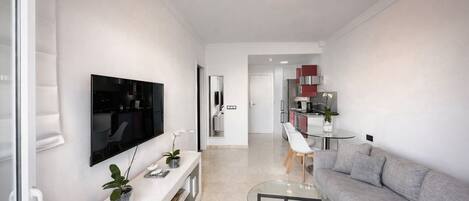 Una sala de estar moderna con un televisor de pantalla plana, una mesa de centro de vidrio, un sofá gris y un comedor con una decoración de color rojo y blanco.