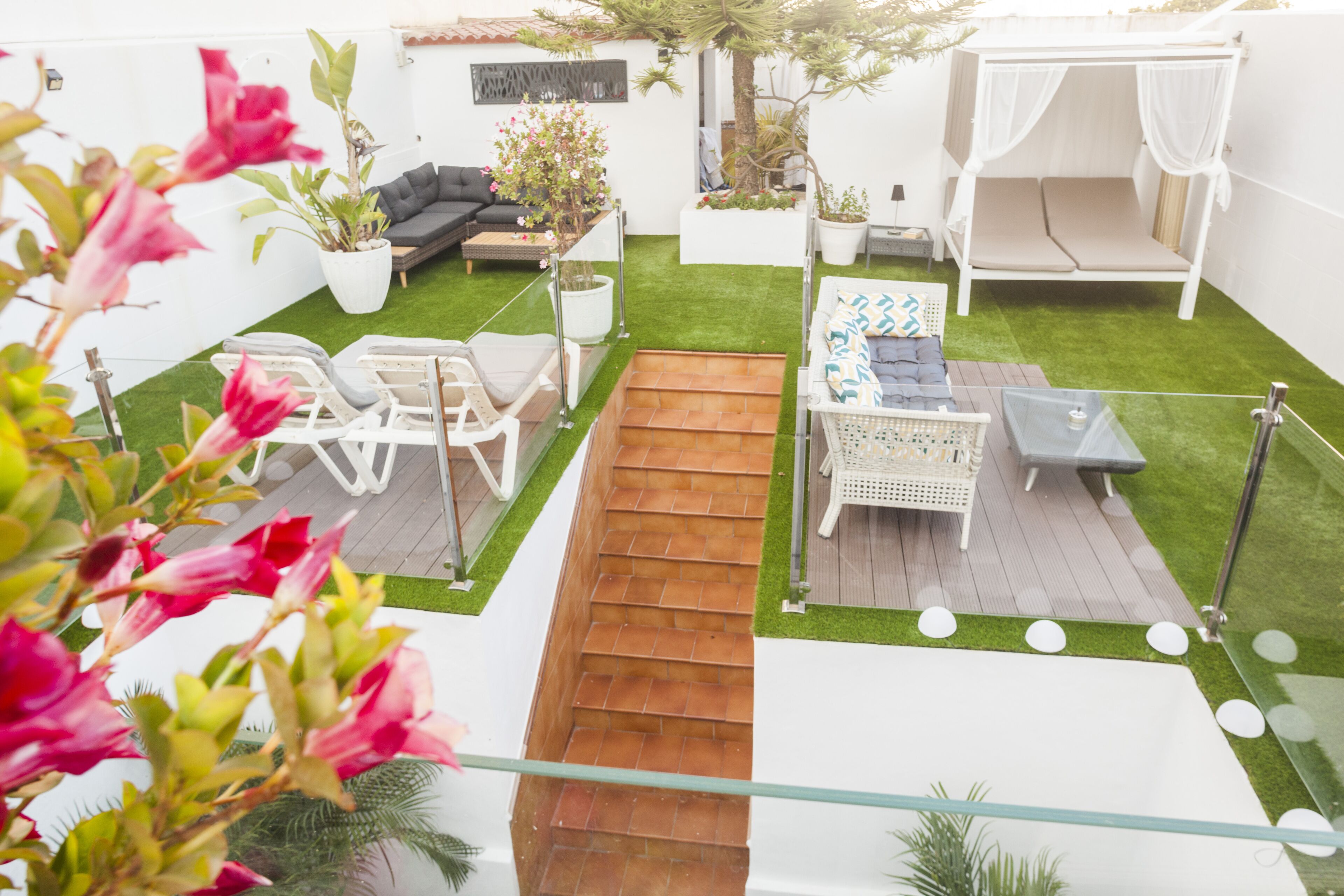 Un patio trasero con una escalera de madera, un sofá blanco, una mesita y una silla blanca.