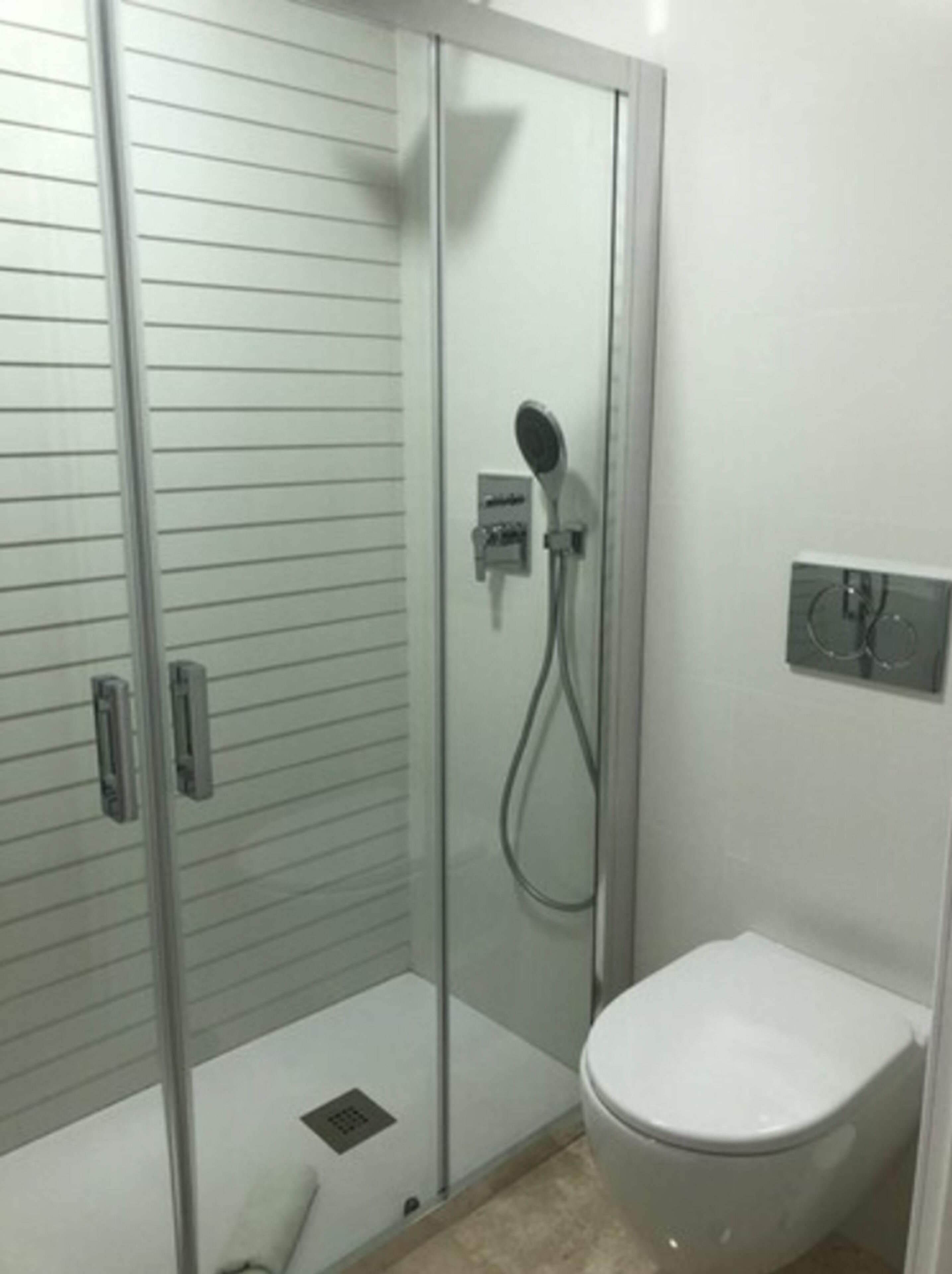 A bathroom with a glass-enclosed shower, a toilet, and a wall-mounted electrical outlet.