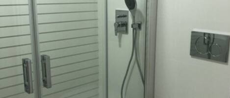 A bathroom with a glass-enclosed shower, a toilet, and a wall-mounted electrical outlet.