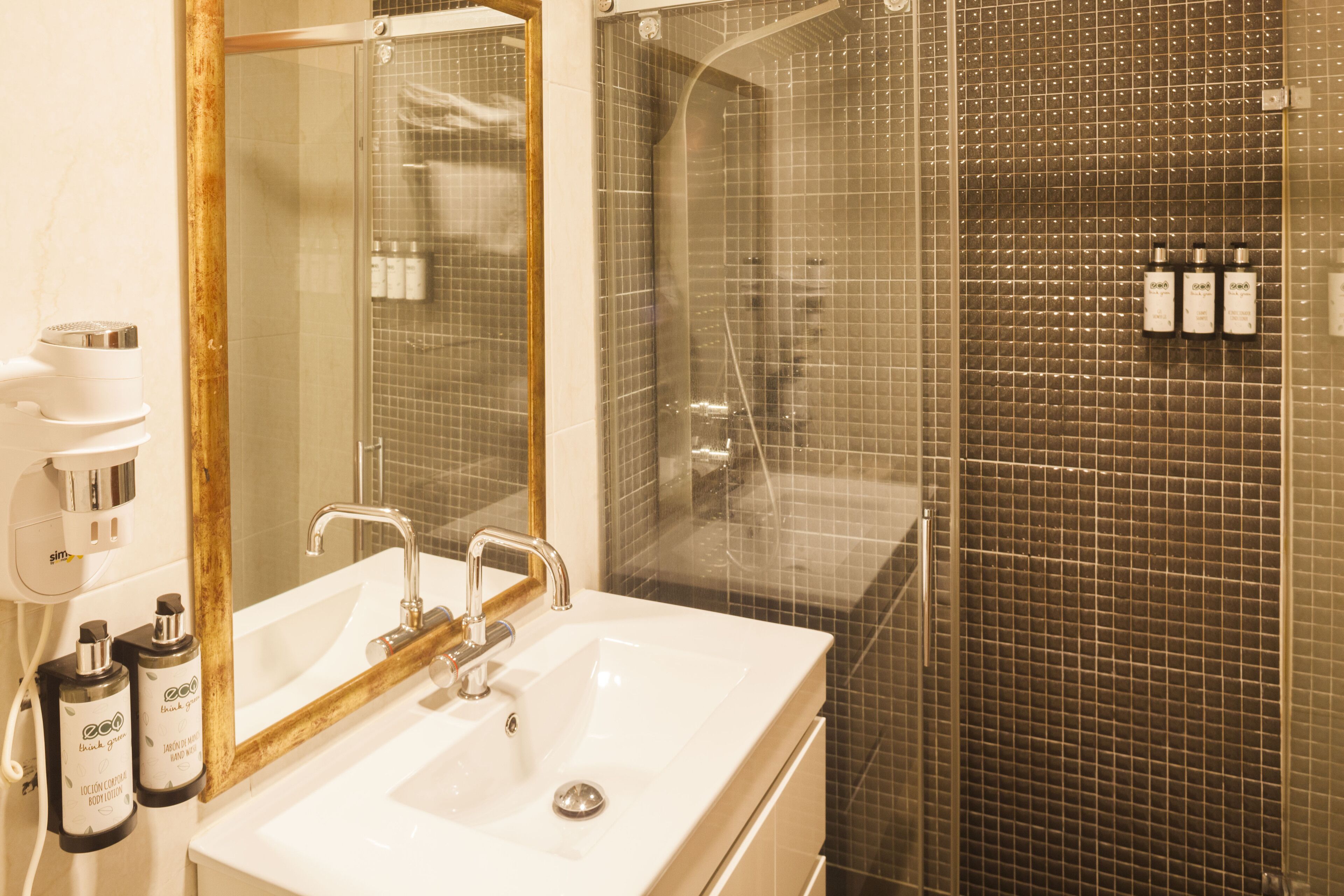 Un baño con lavamanos blanco, espejo y zona de ducha con pared de azulejos.