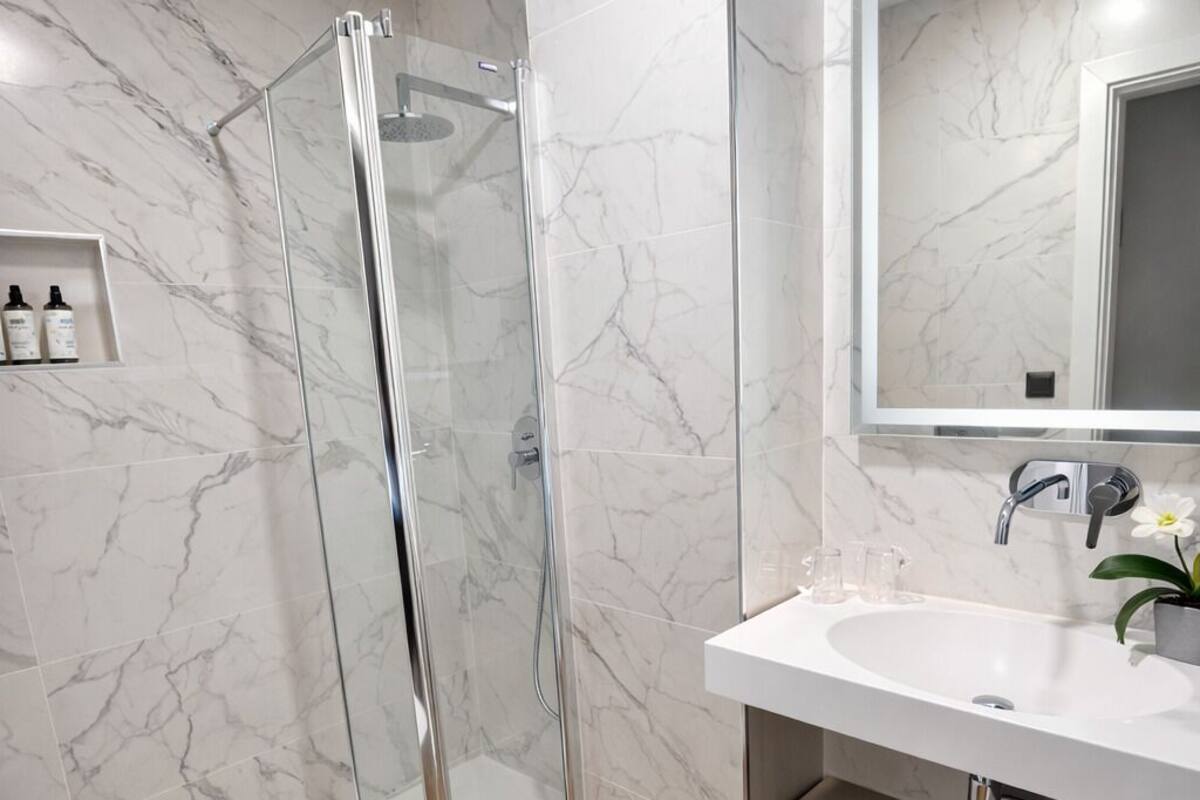 Un baño moderno con cabina de ducha de vidrio, inodoro blanco, lavamanos con espejo y tocador con toallero.