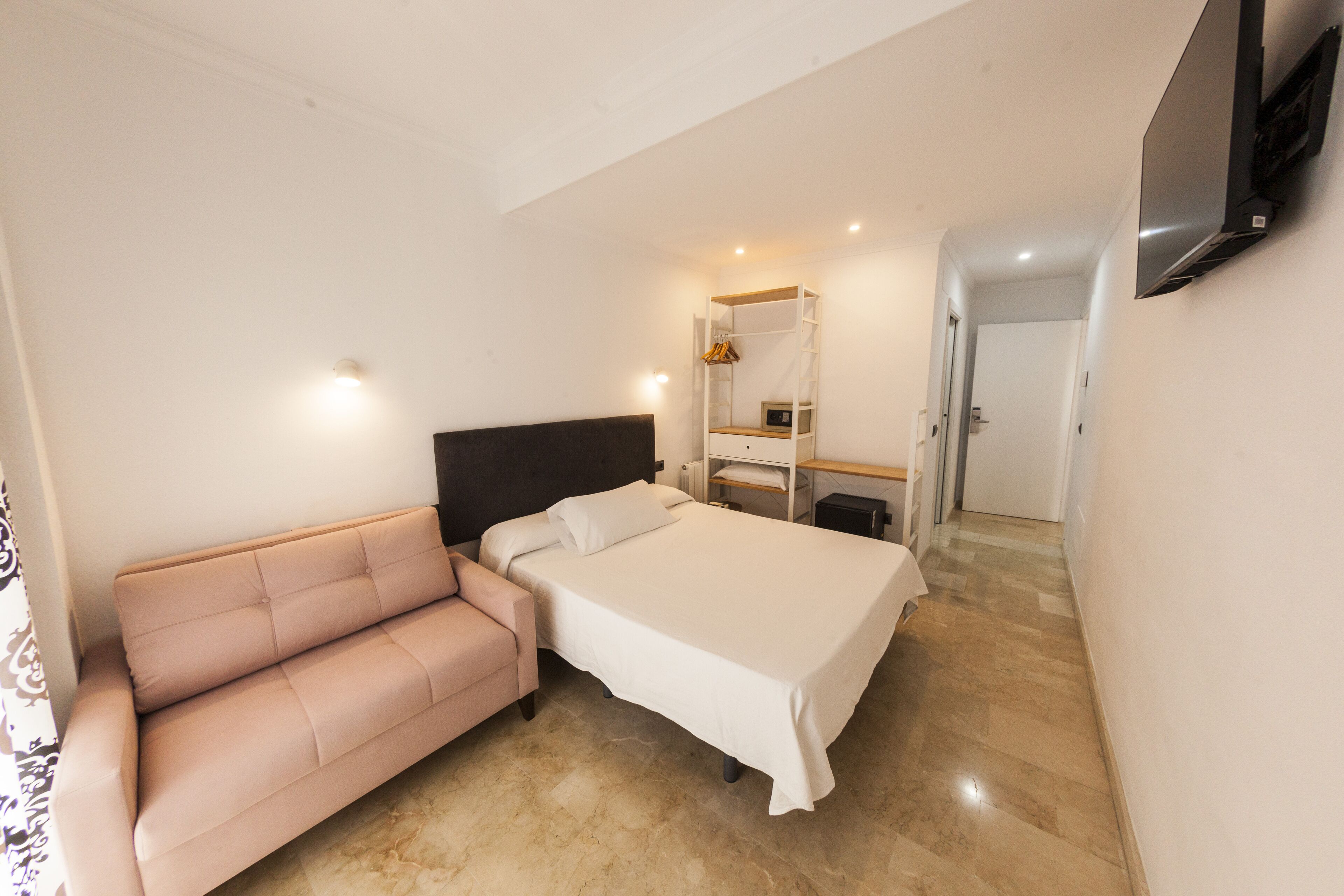 A bedroom with a bed, a sofa, a wardrobe, and a television mounted on the wall.