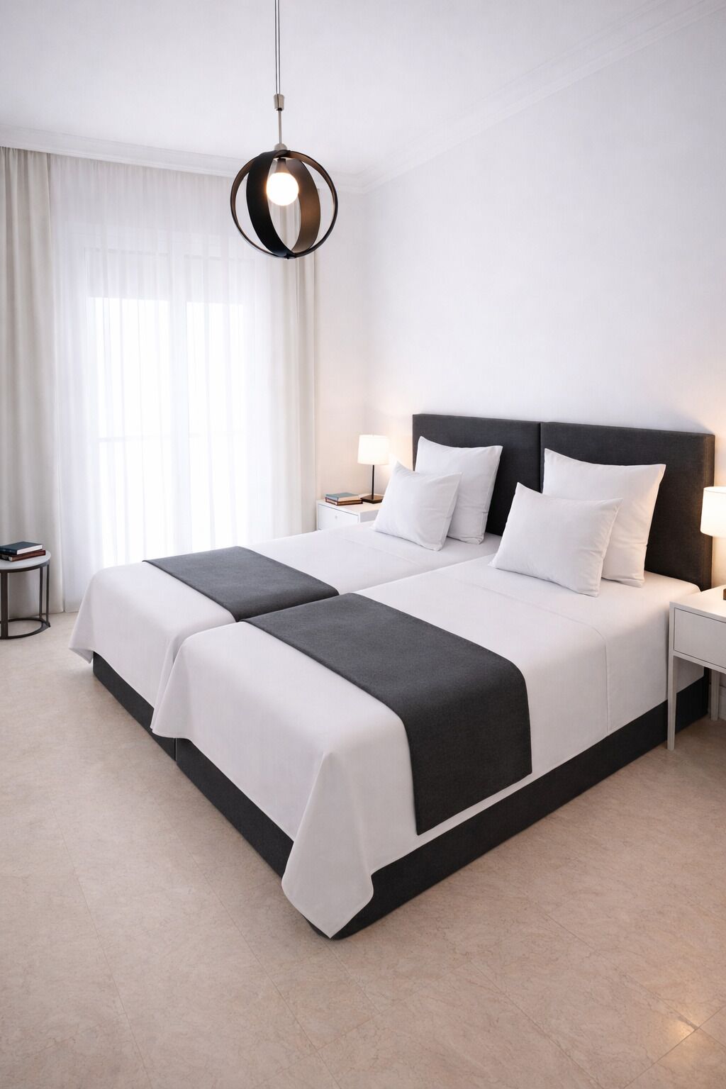 A double bed with white and black bedding, a round pendant light, a bedside table with a lamp, and a nightstand with a book.