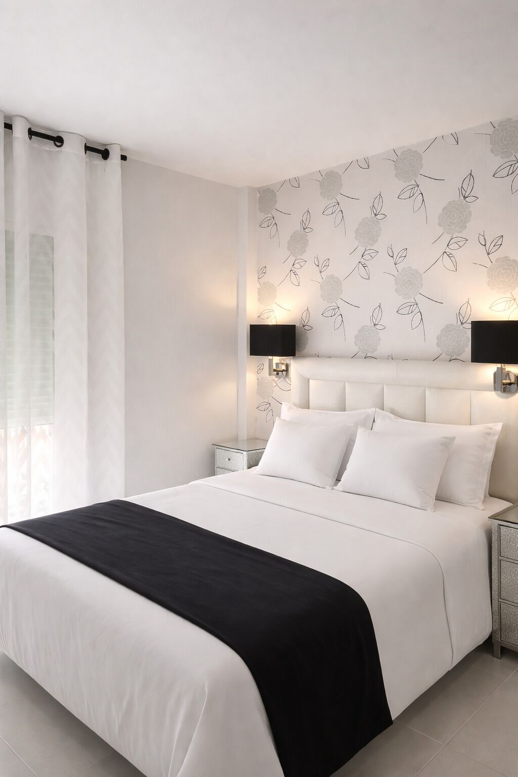 Un dormitorio moderno con una cama grande, ropa de cama blanca, un plaid negro y un papel tapiz con estampado floral.