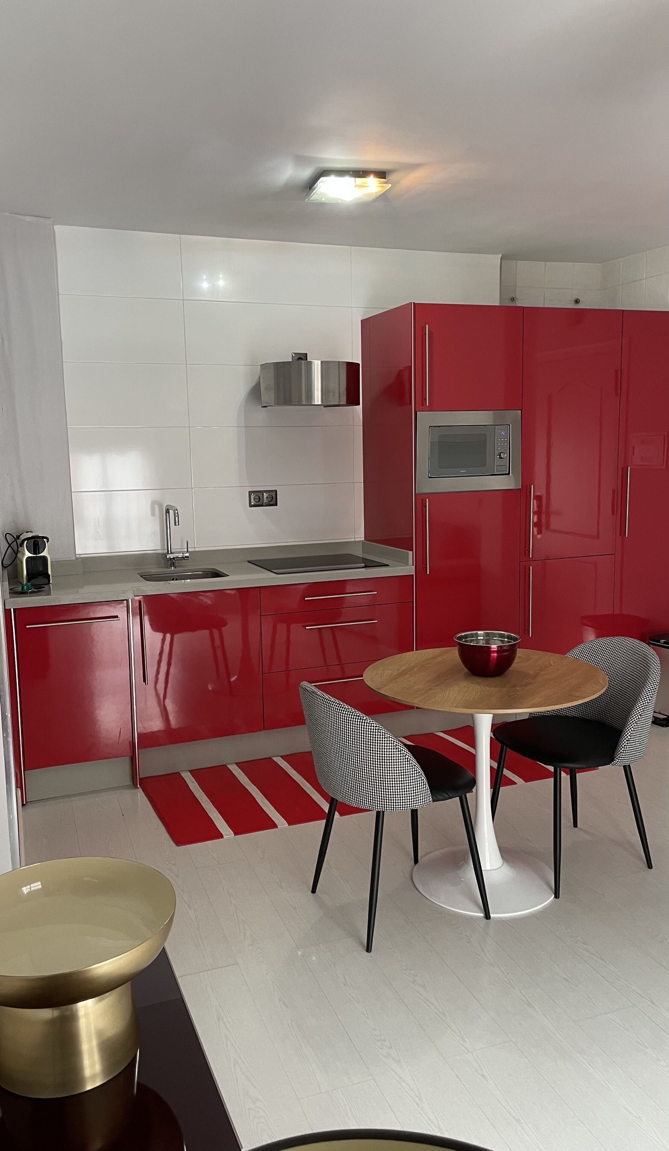 Une cuisine moderne avec des meubles de rangement rouges, un four à micro-ondes en acier inoxydable et un coin repas comprenant une table ronde et deux chaises.