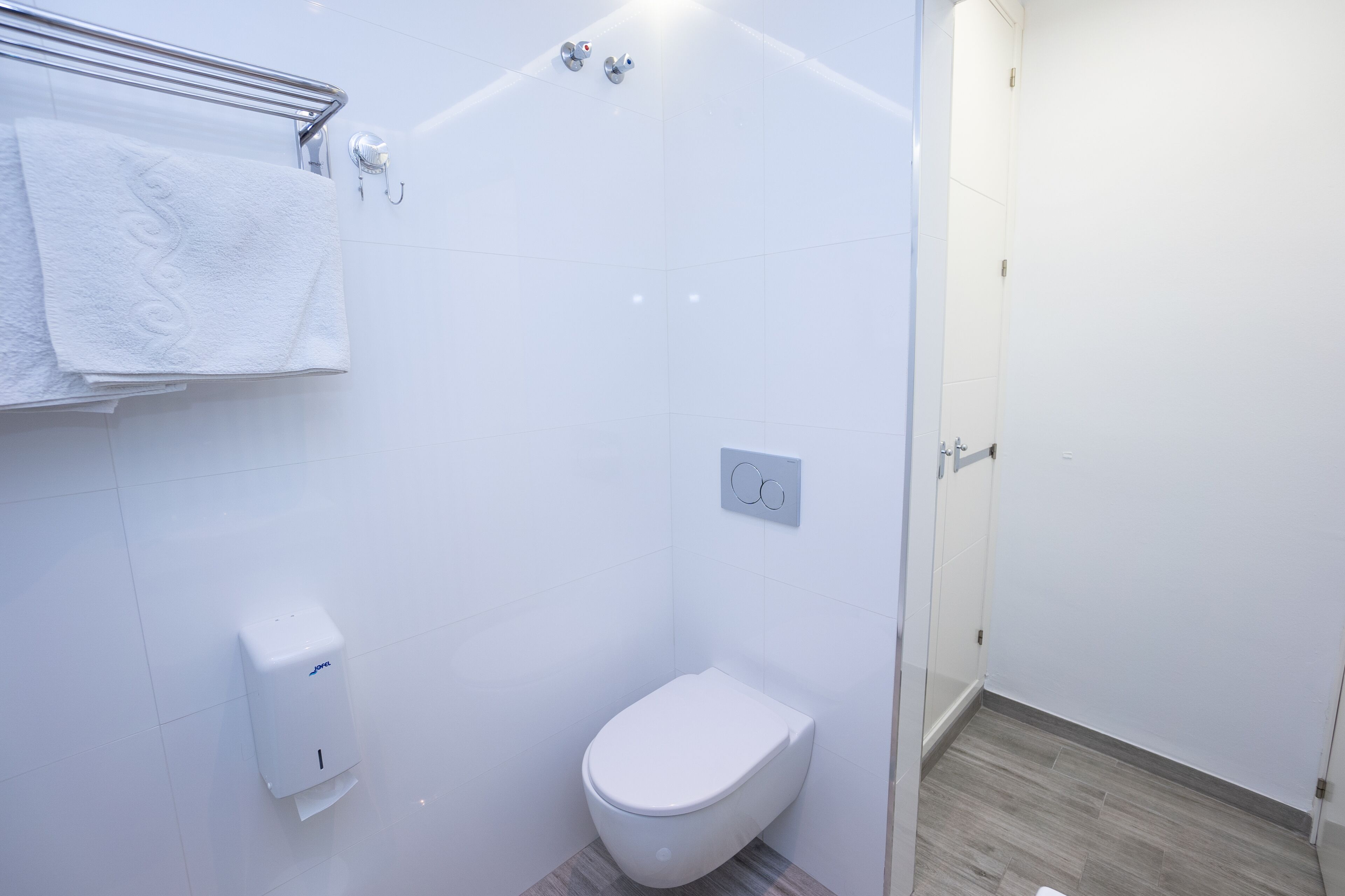 Une petite salle de bain moderne avec des toilettes blanches, un sèche-mains et un porte-serviettes.