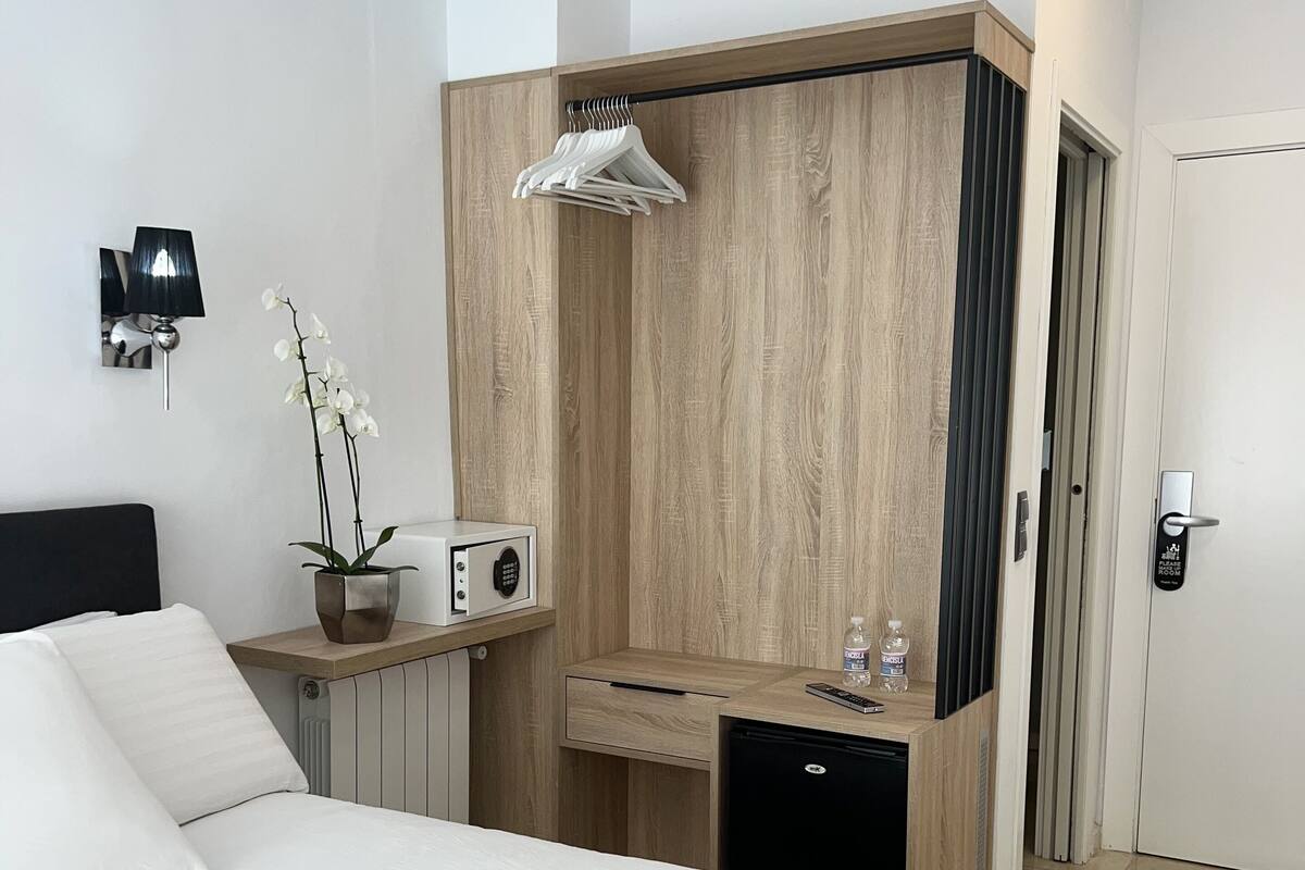 Una habitación de hotel moderna con cama, escritorio, armario, una pequeña mesa con lámpara y televisor montado en la pared.
