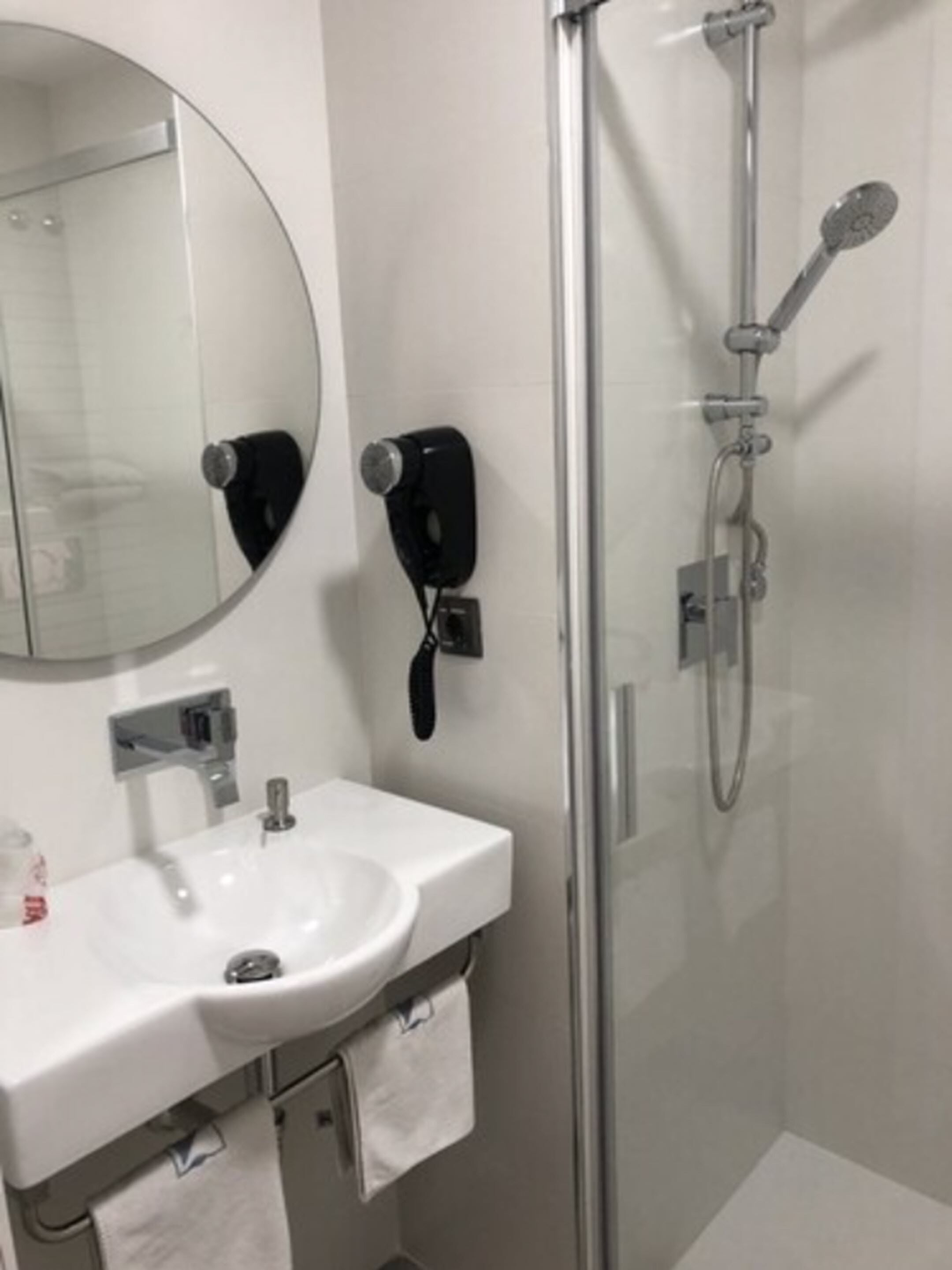 Une salle de bain avec un miroir rond, un lavabo, une douchette à main et un sèche-cheveux.
