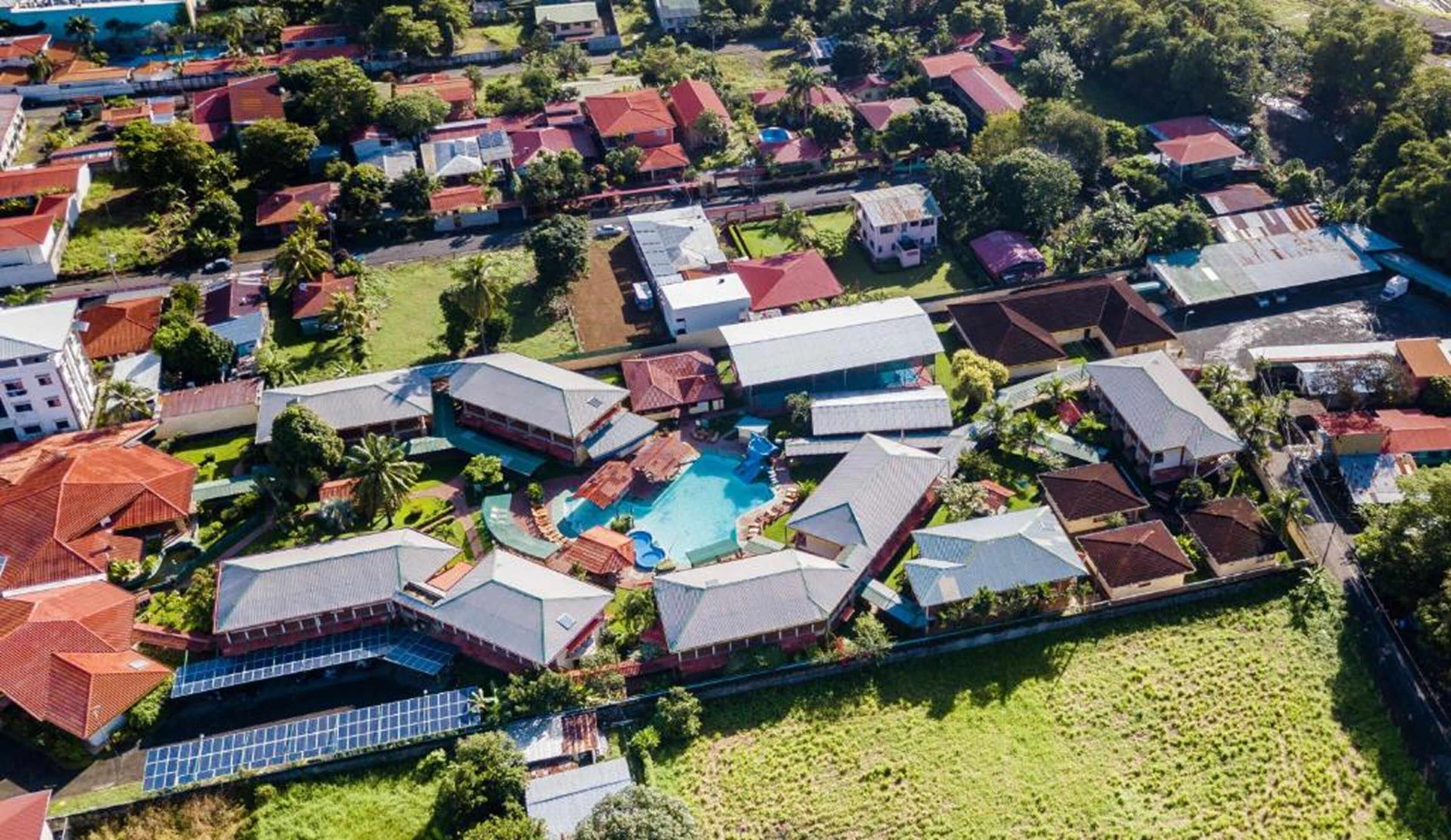 An aerial view of a residential area with houses, a swimming pool, and solar panels.