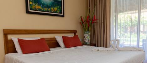 A neatly made bed with red and white pillows, a painting above it, and a vase with red flowers on the nightstand.