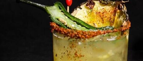 Cóctel con un chile verde y una cereza roja como adorno, servido en un vaso con borde salado.