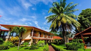 Un hotel con un edificio a tetto rosso, una palma e un giardino curato.