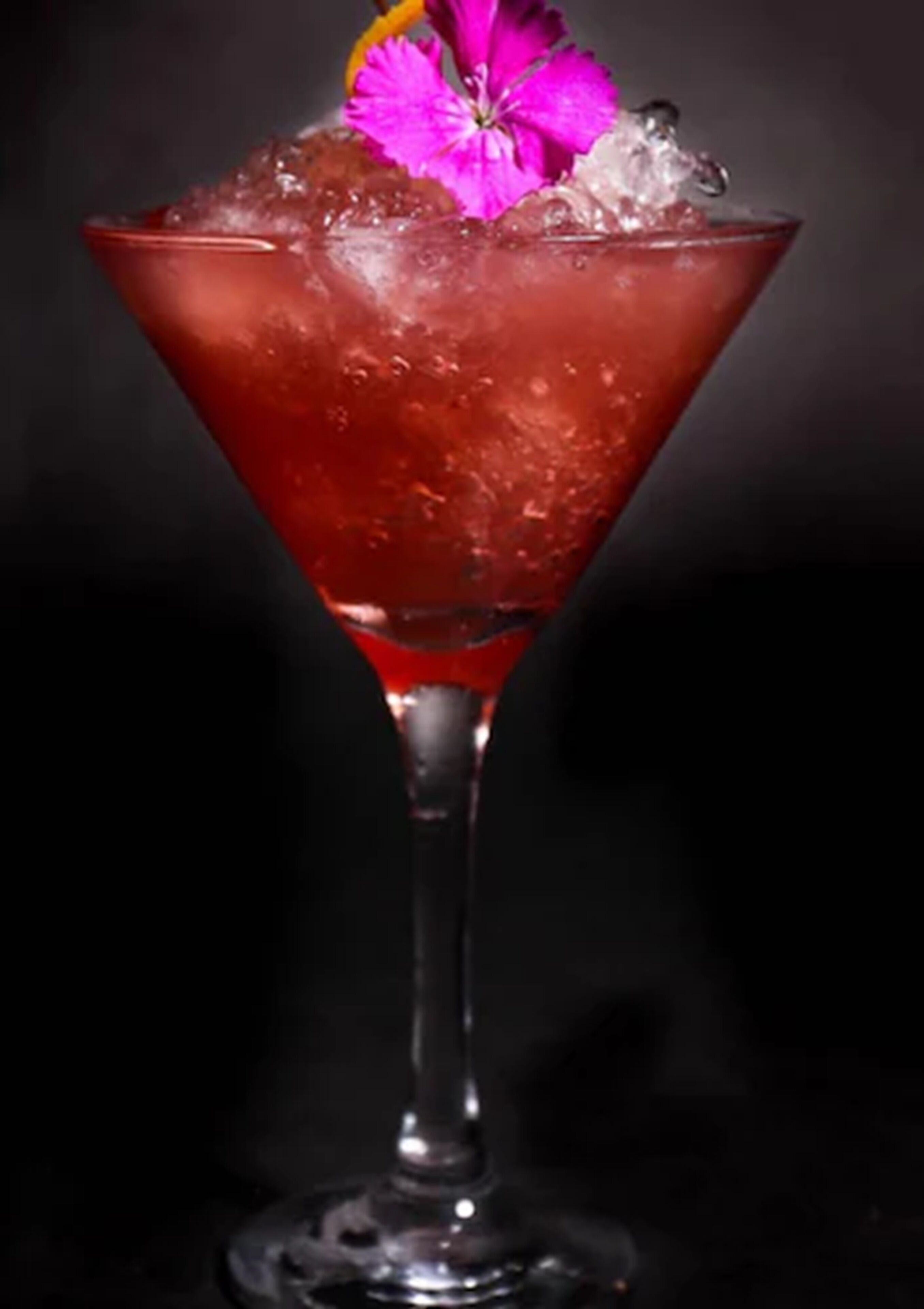 A martini glass with a red liquid, ice cubes, and a pink flower garnish.