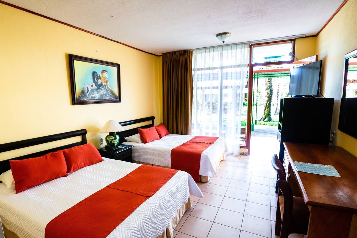 A hotel room with two beds, a television, a desk, and a painting on the wall.