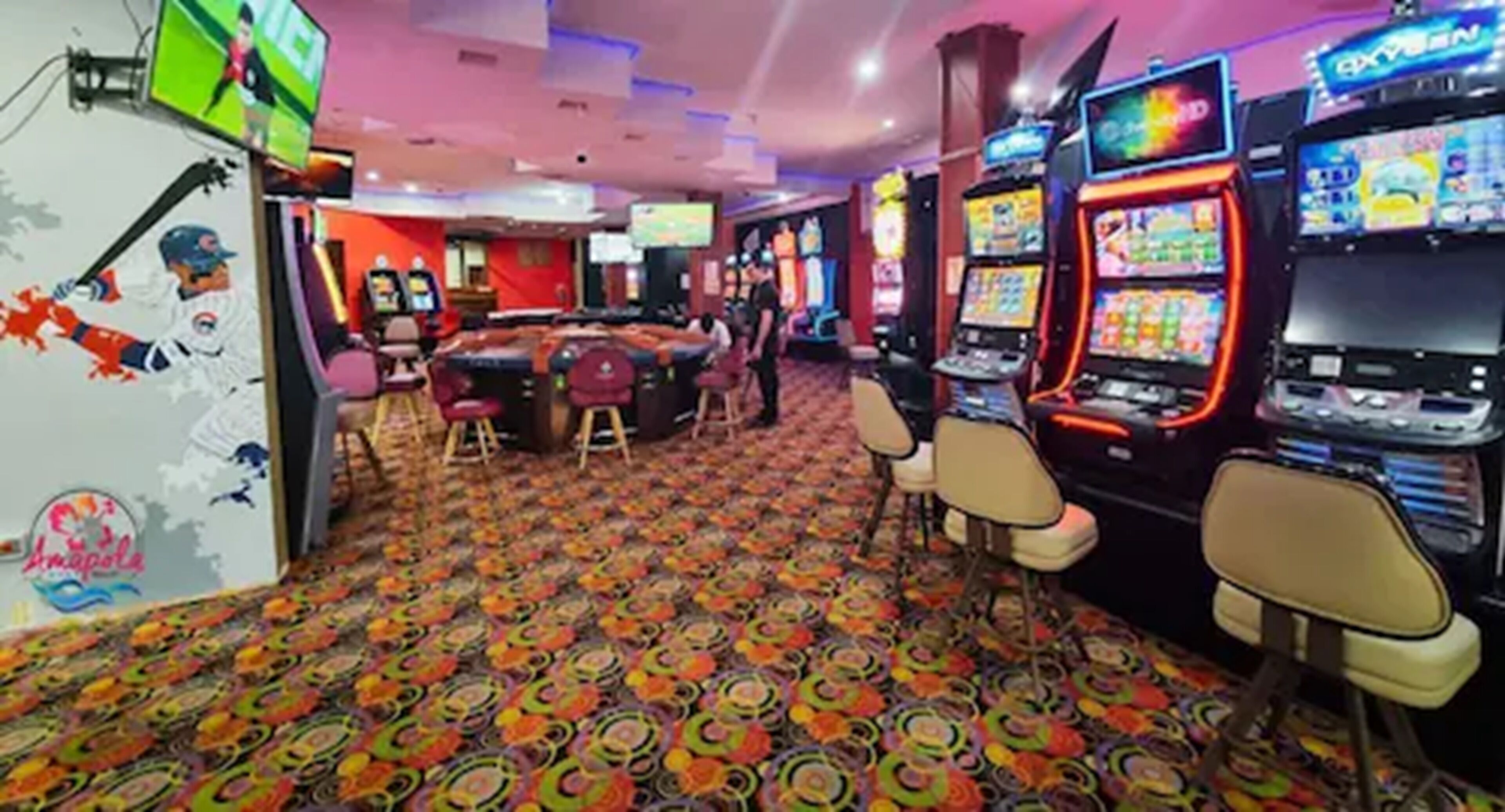 Een casino-interieur met gokkasten, een bar en een vloerkleed met dessin.