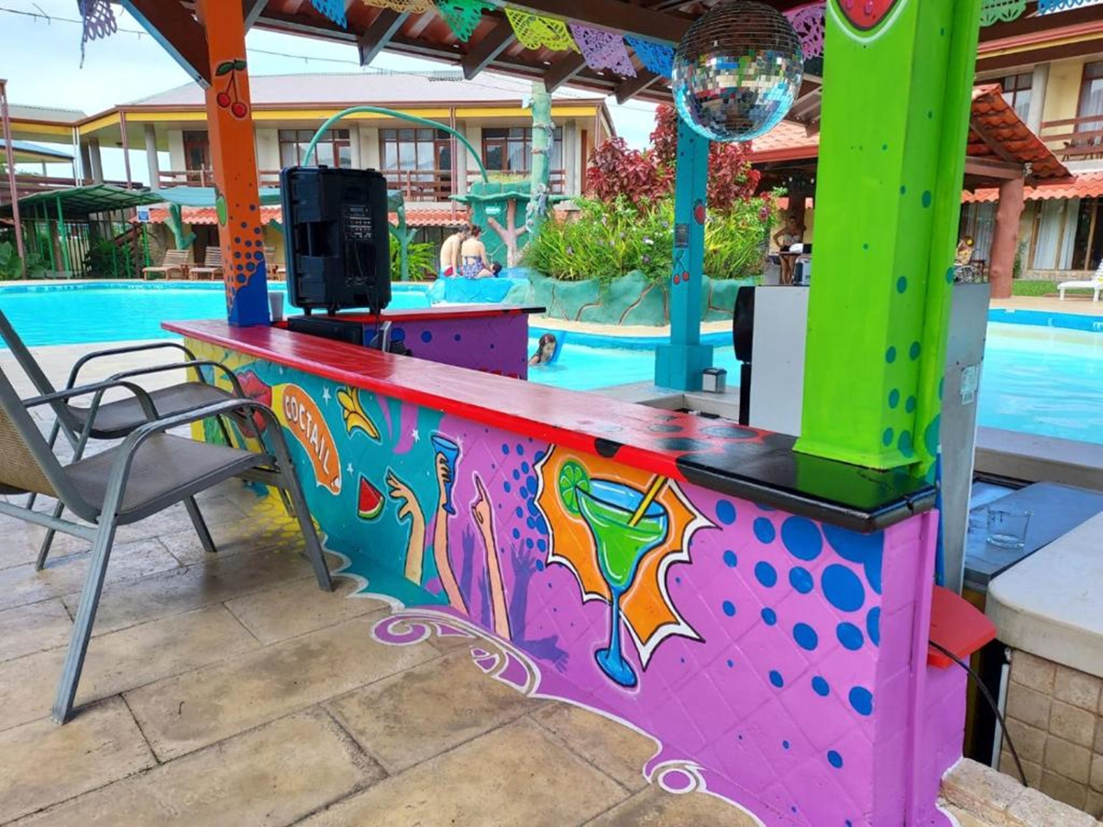 A colorful poolside bar with a mural, a disco ball, and a pool in the background.