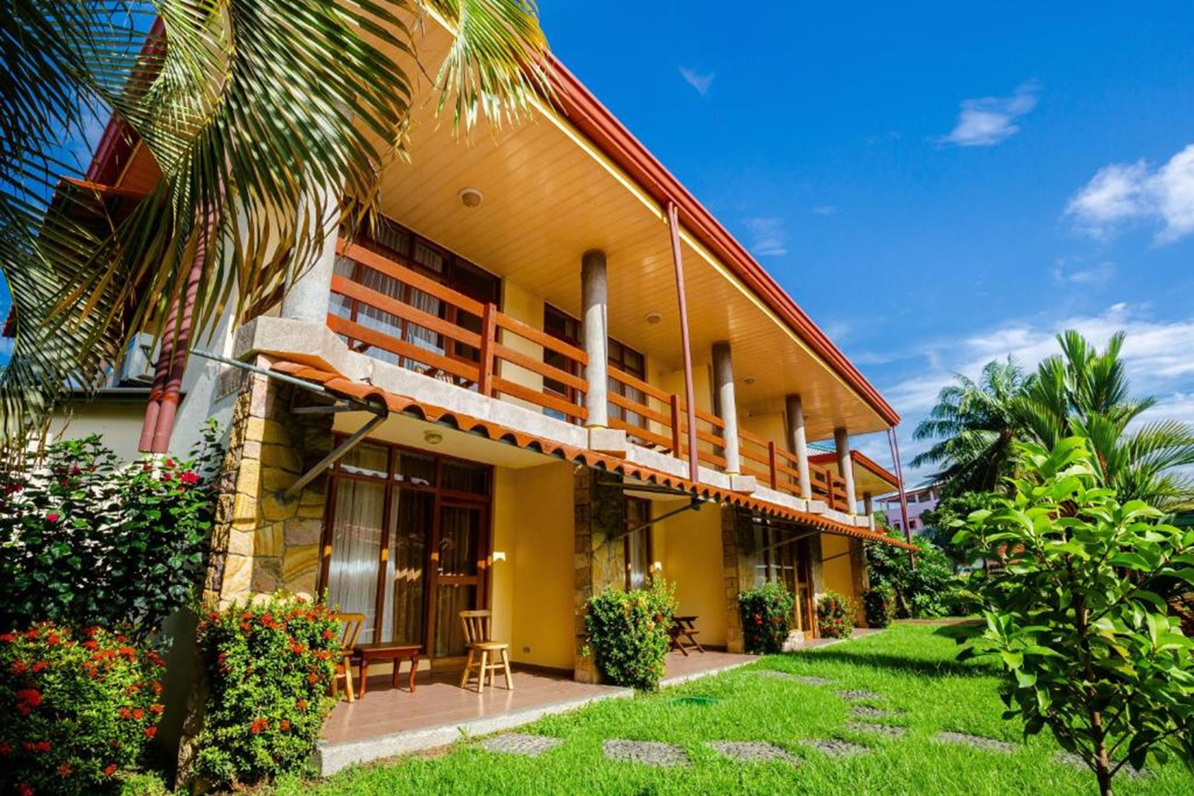 A two-story building with a balcony, surrounded by lush greenery and palm trees.