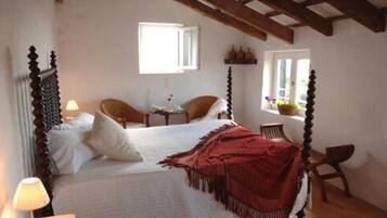 A bedroom with a four-poster bed, a small table with a chair, and a window with a view of the outside.