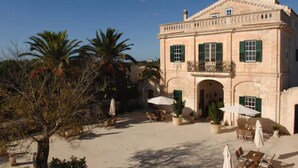A large, historic building with a courtyard, featuring outdoor seating and palm trees. -  Alcaufar Vell Hotel Rural & Restaurant (Sant Lluis)