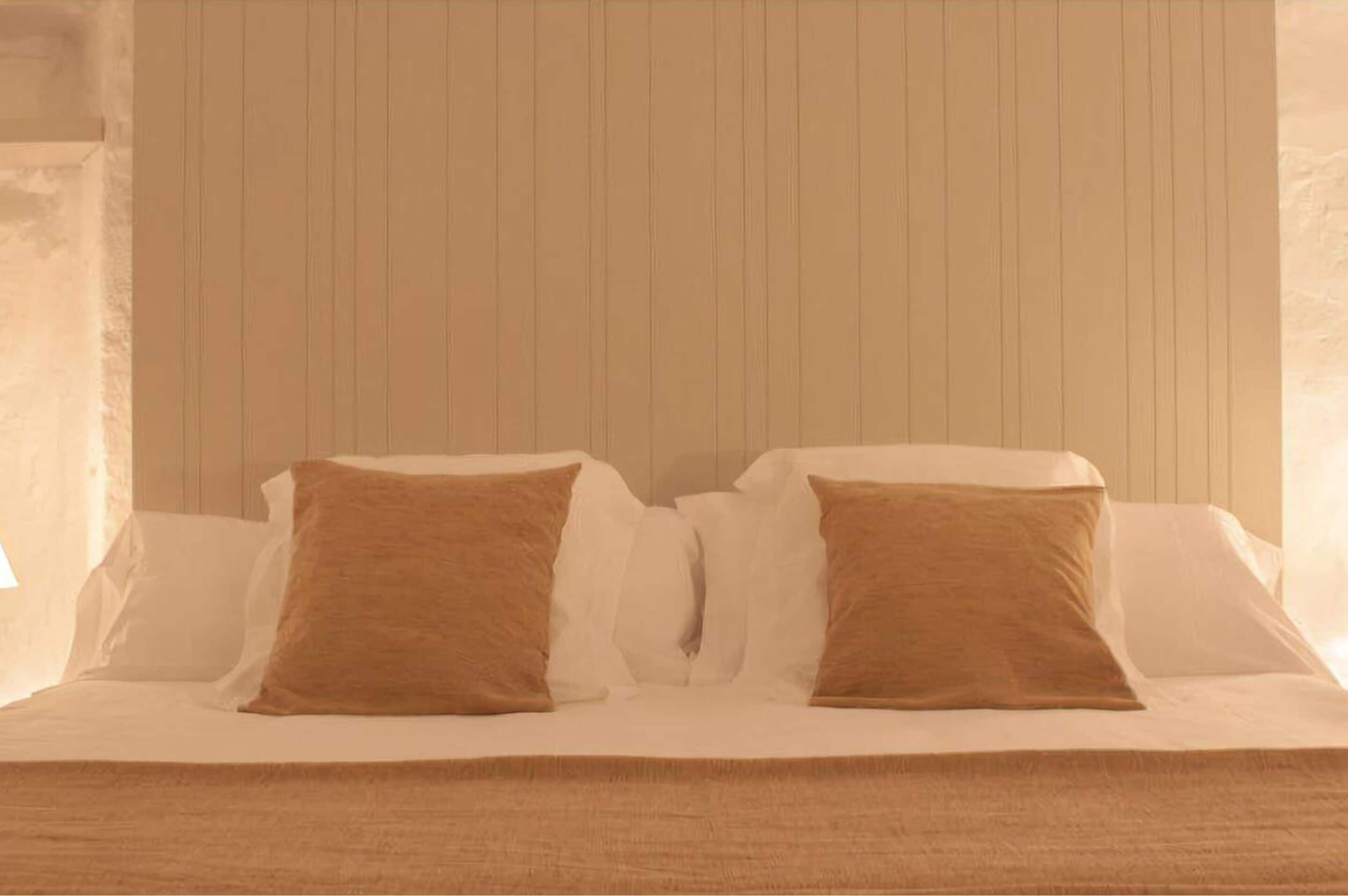 Una cama con ropa blanca y dos almohadas marrones.